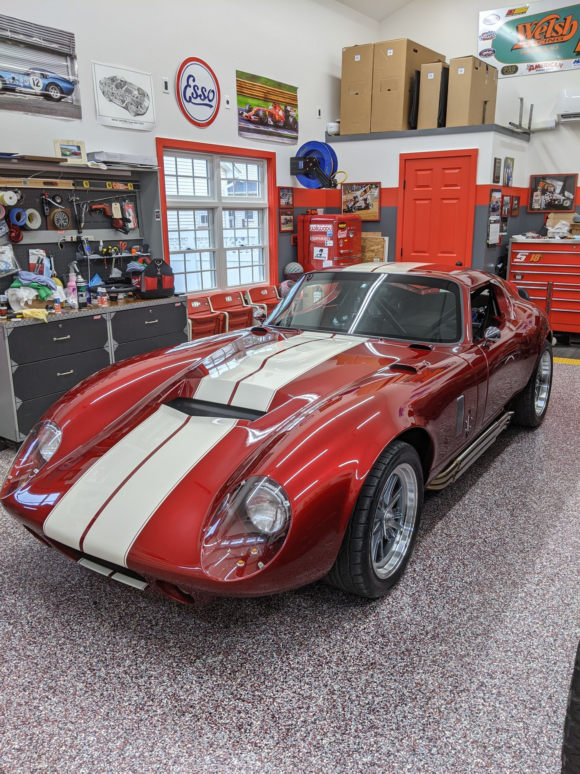 Red vintage sports car with white racing stripes in a garage workshop