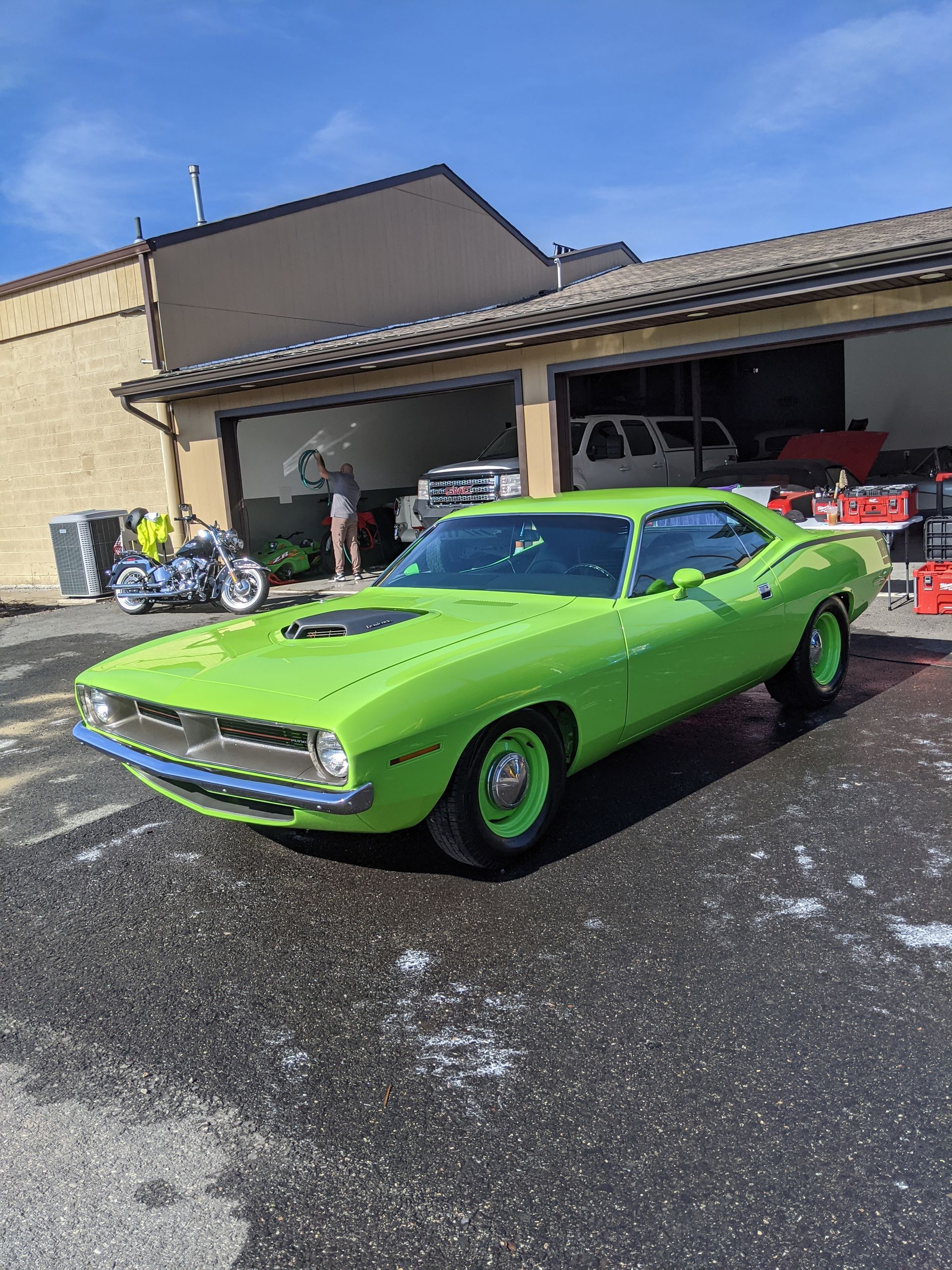 Bright green classic muscle car parked outside a garage, with motorcycles and a red SUV nearby.