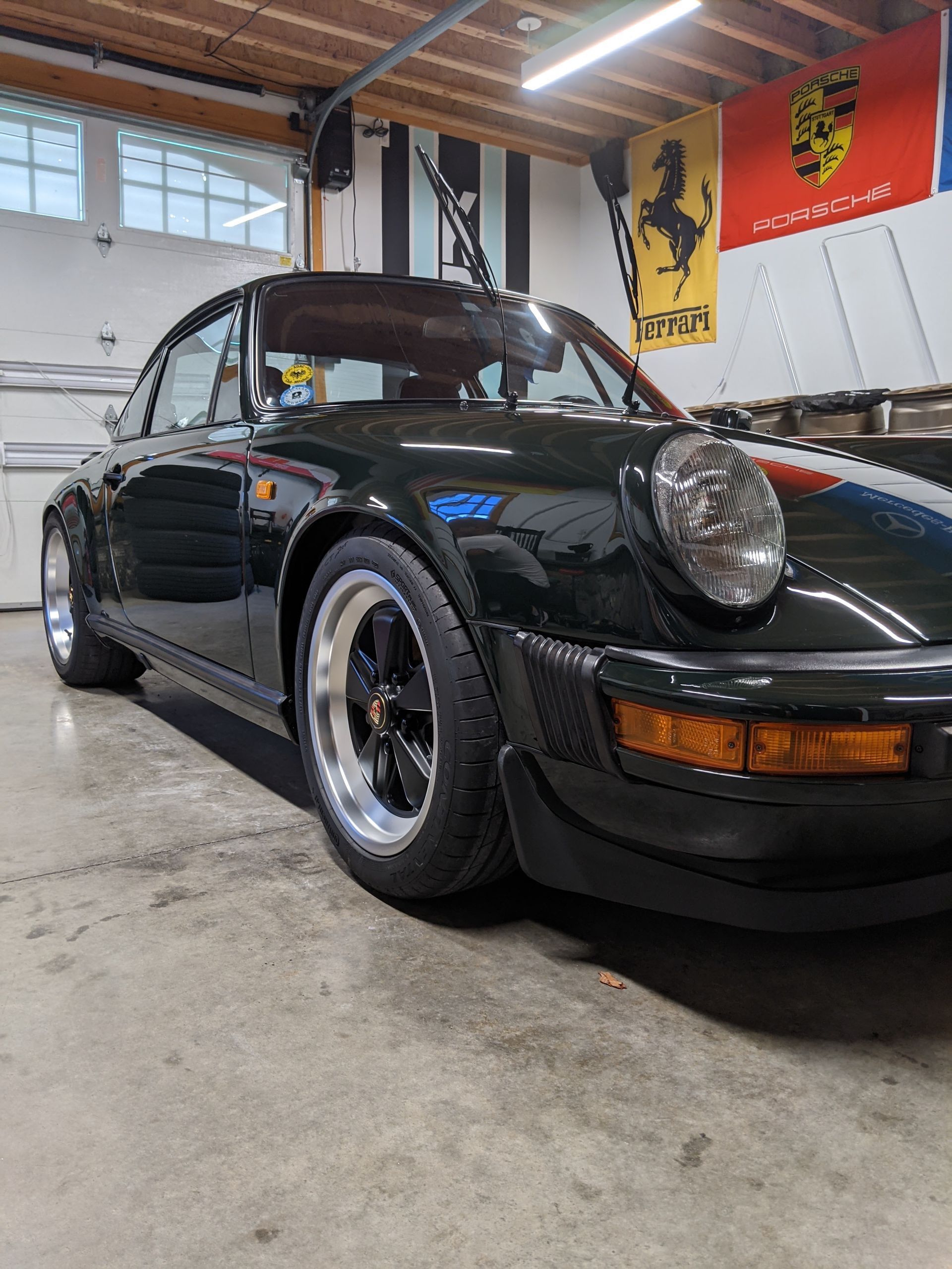 Black classic Porsche 911 in a garage, front three-quarter view with polished wheels and pop-up headlights.