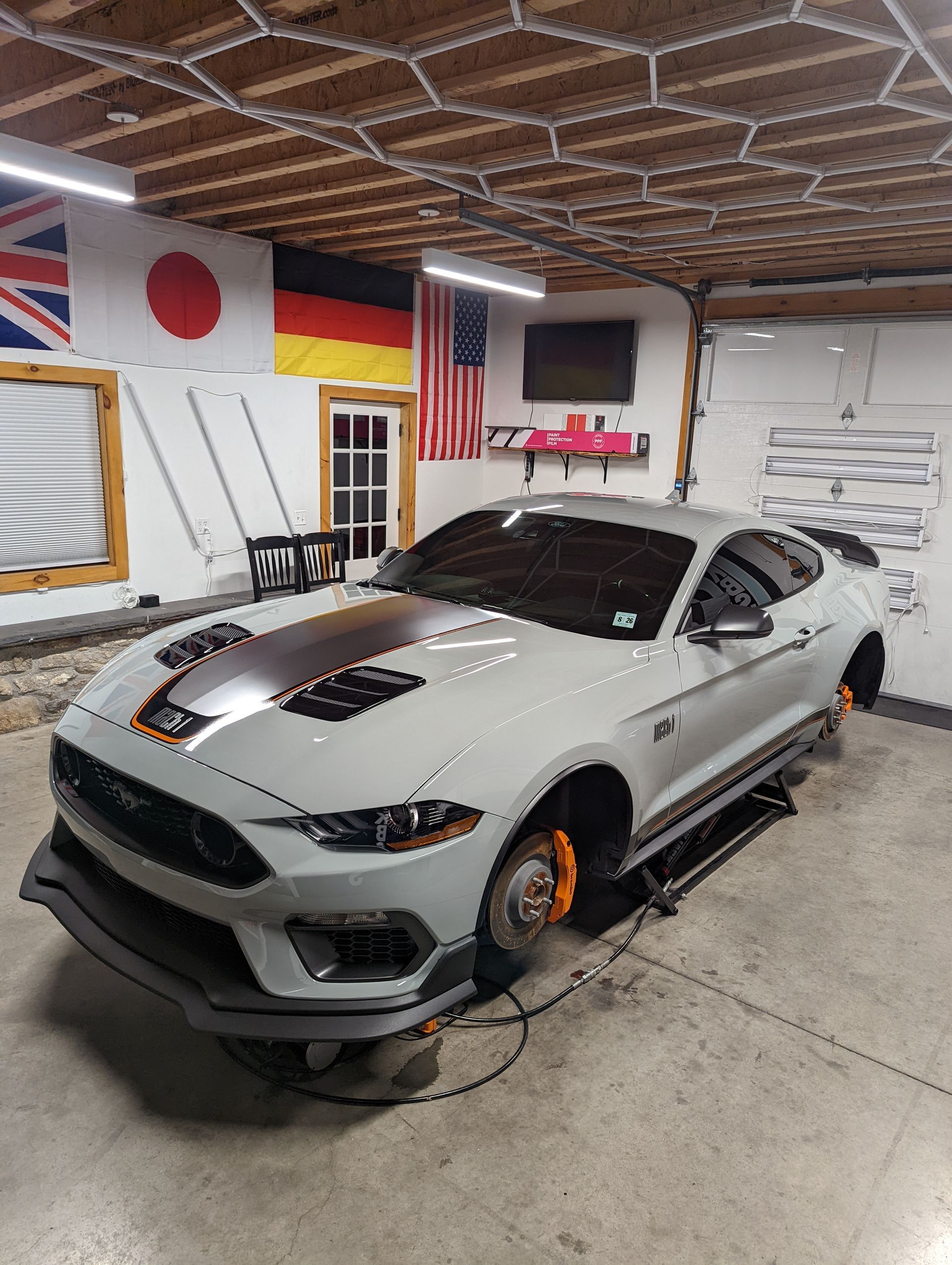White sports car with black racing stripes in a garage, with flags on the wall and orange brake calipers