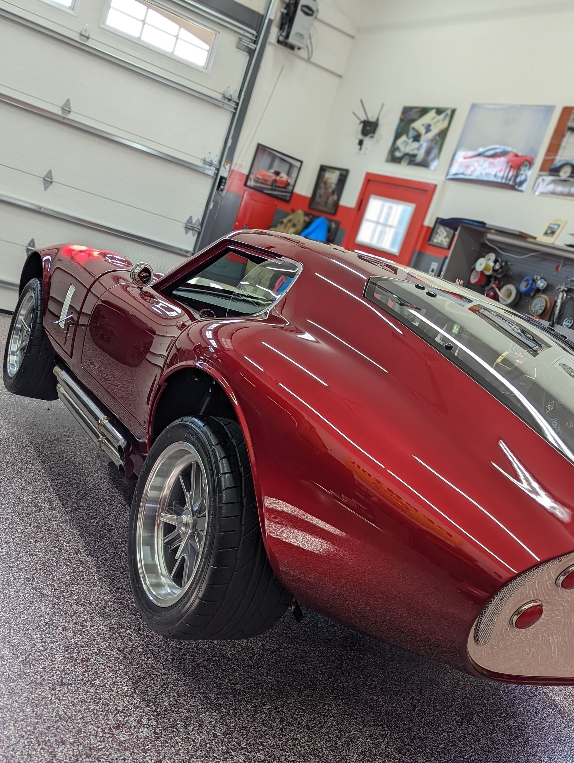 Red classic sports car in a garage, shown from the rear side with glossy maroon paint and chrome wheels