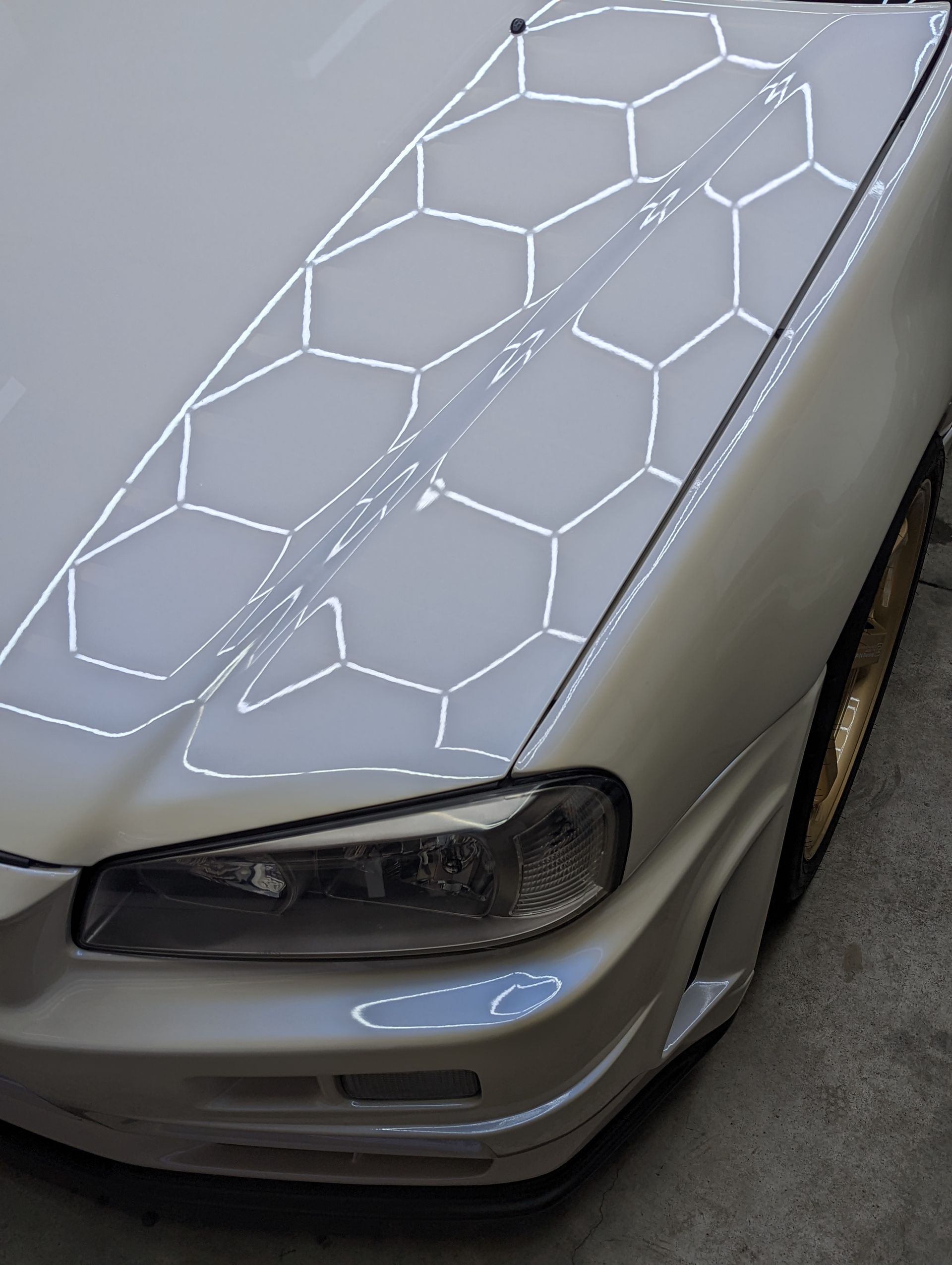 Silver sports car hood with a glowing hexagonal light pattern and a black headlight detail.