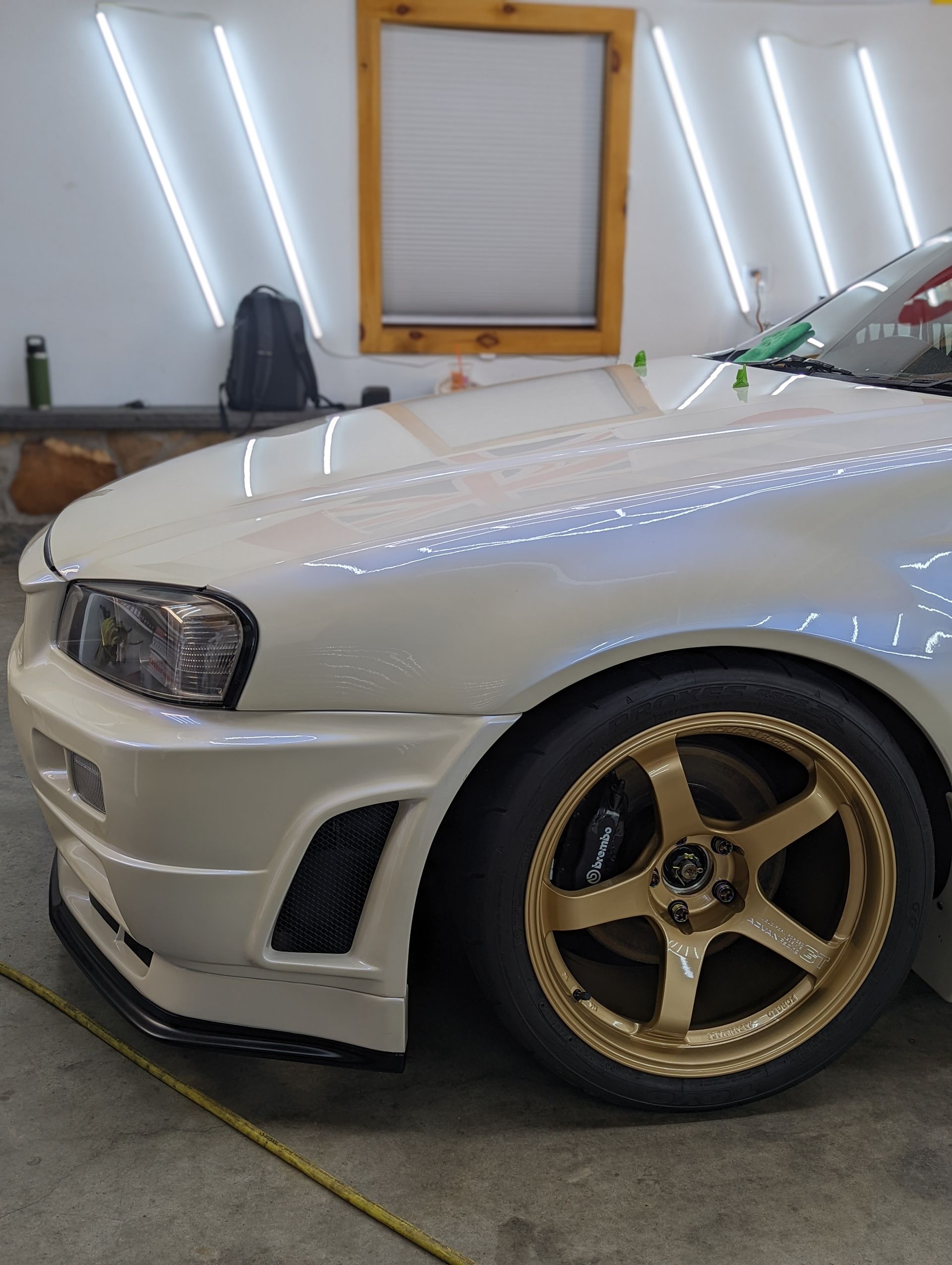 White sports car with gold rims parked in a garage under bright wall lights.