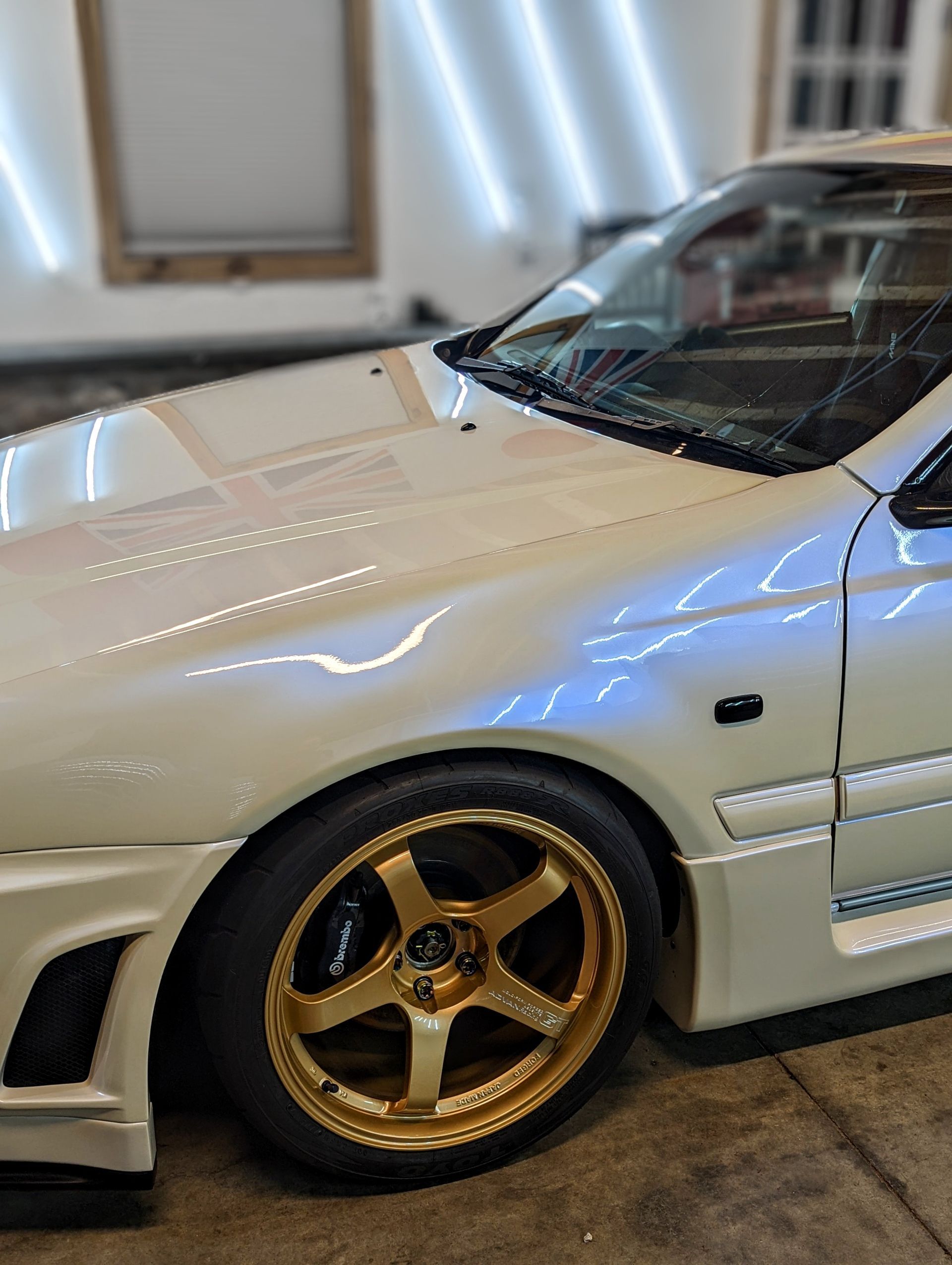 White sports car with gold rims parked in a garage, close-up of the front side.