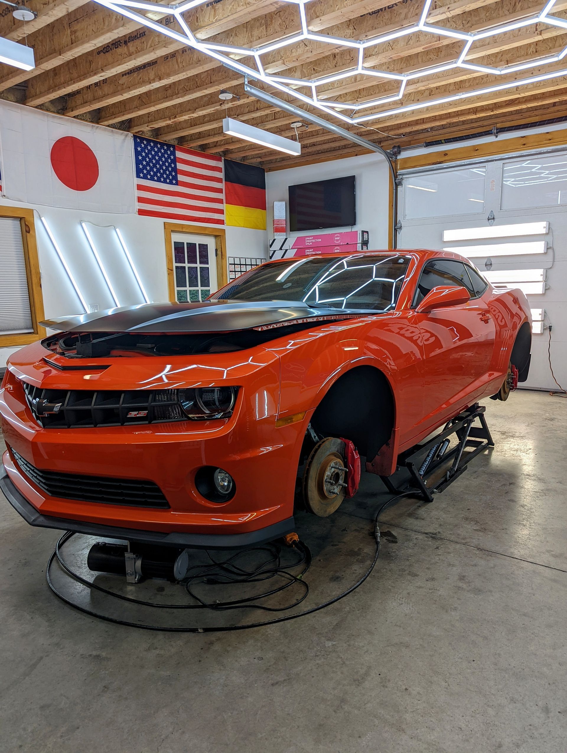 Orange sports car on a turntable in an auto shop, with flags and garage lights overhead.