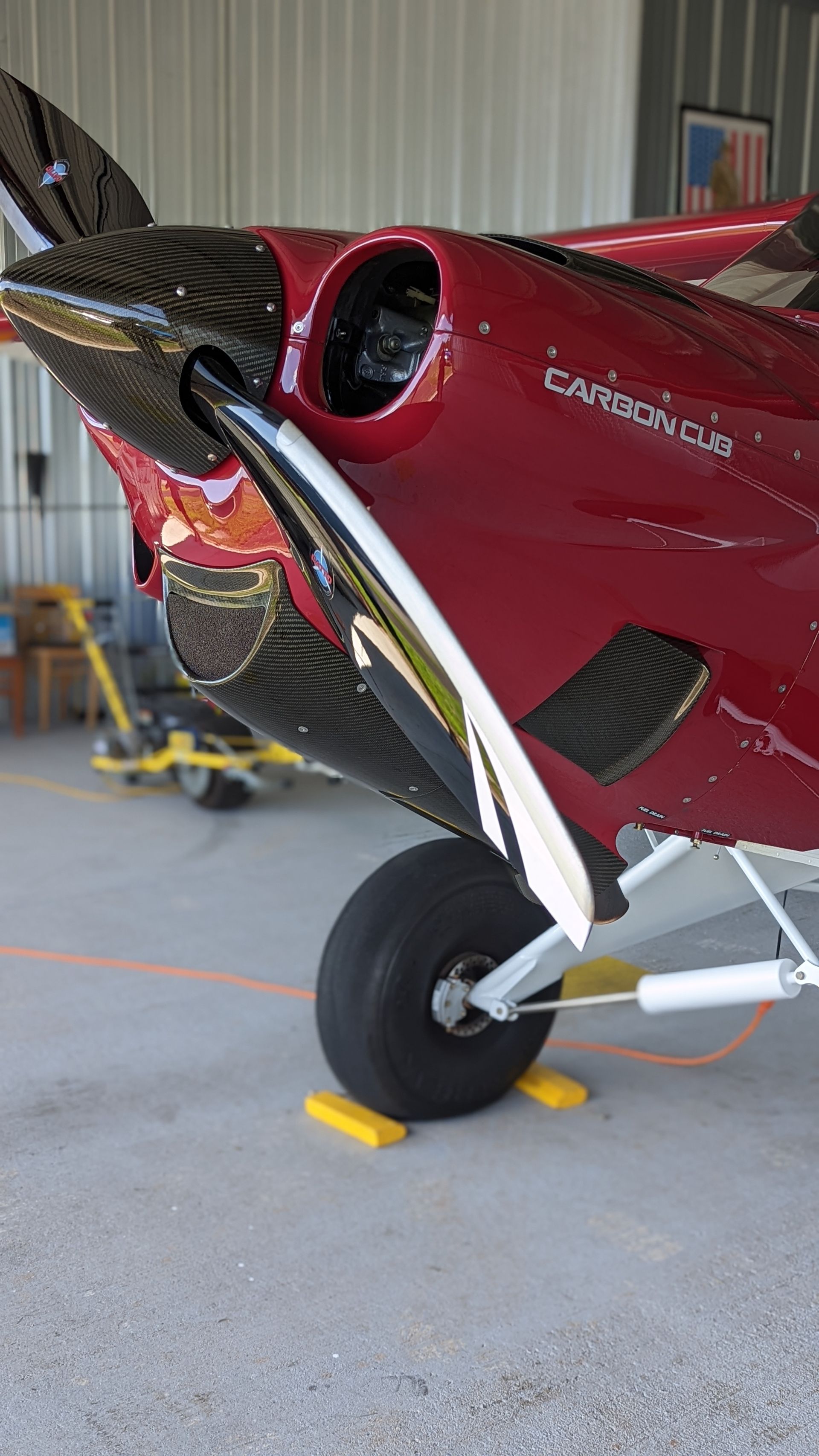 Red single-engine airplane nose and front wheel inside a hangar