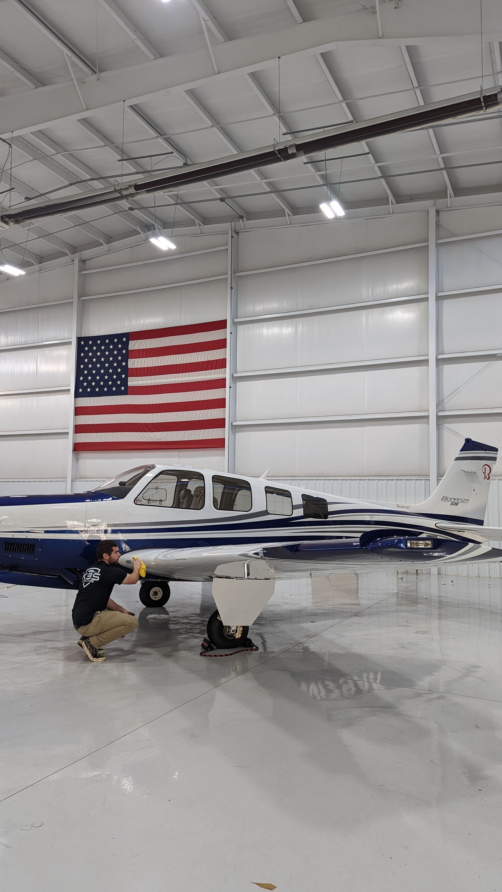 Small blue-and-white airplane in a hangar with a large U.S. flag on the wall