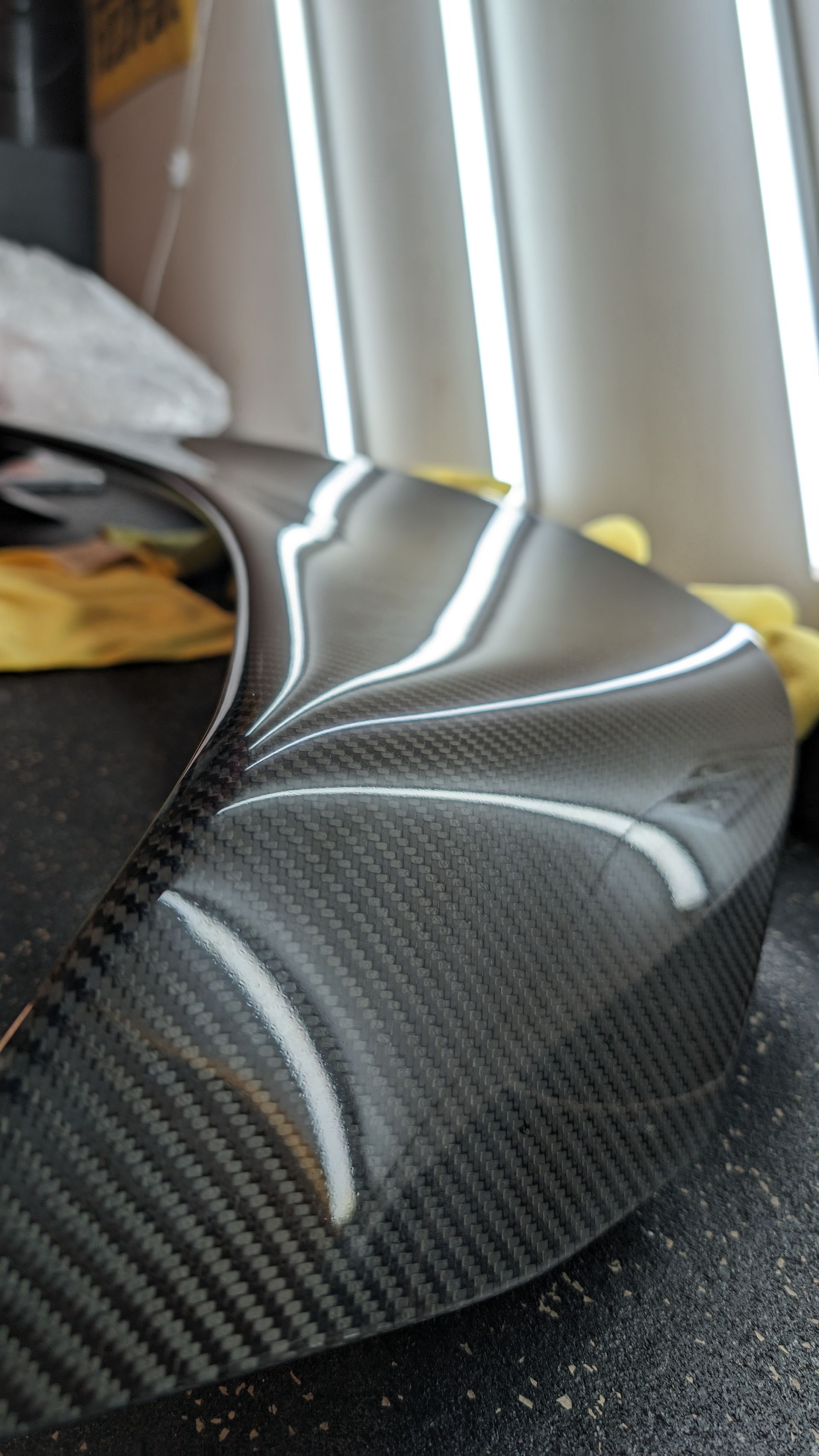 Carbon fiber car body panel close-up reflecting light indoors