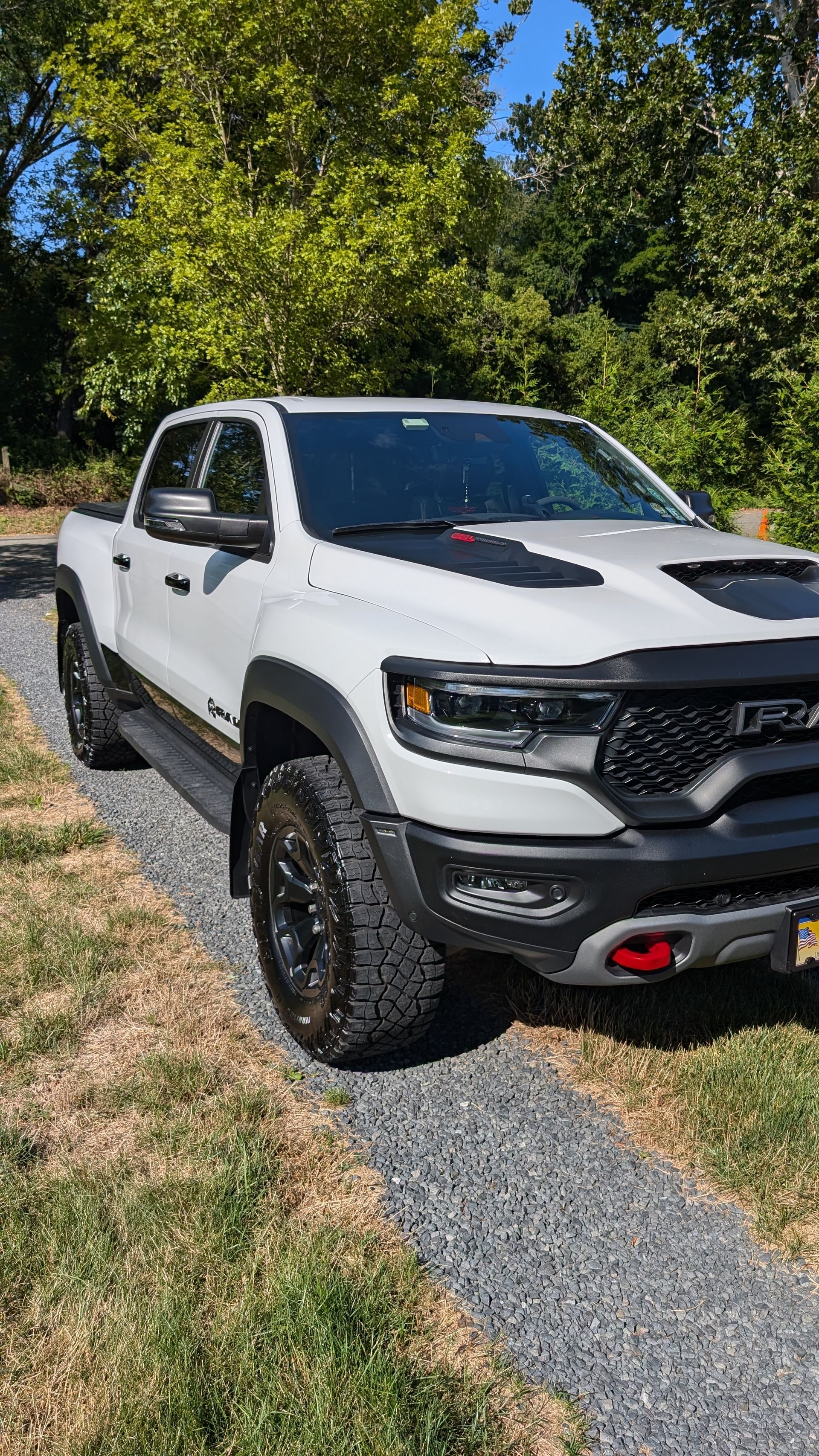 White pickup truck parked on a gravel path beside grass and trees in sunlight