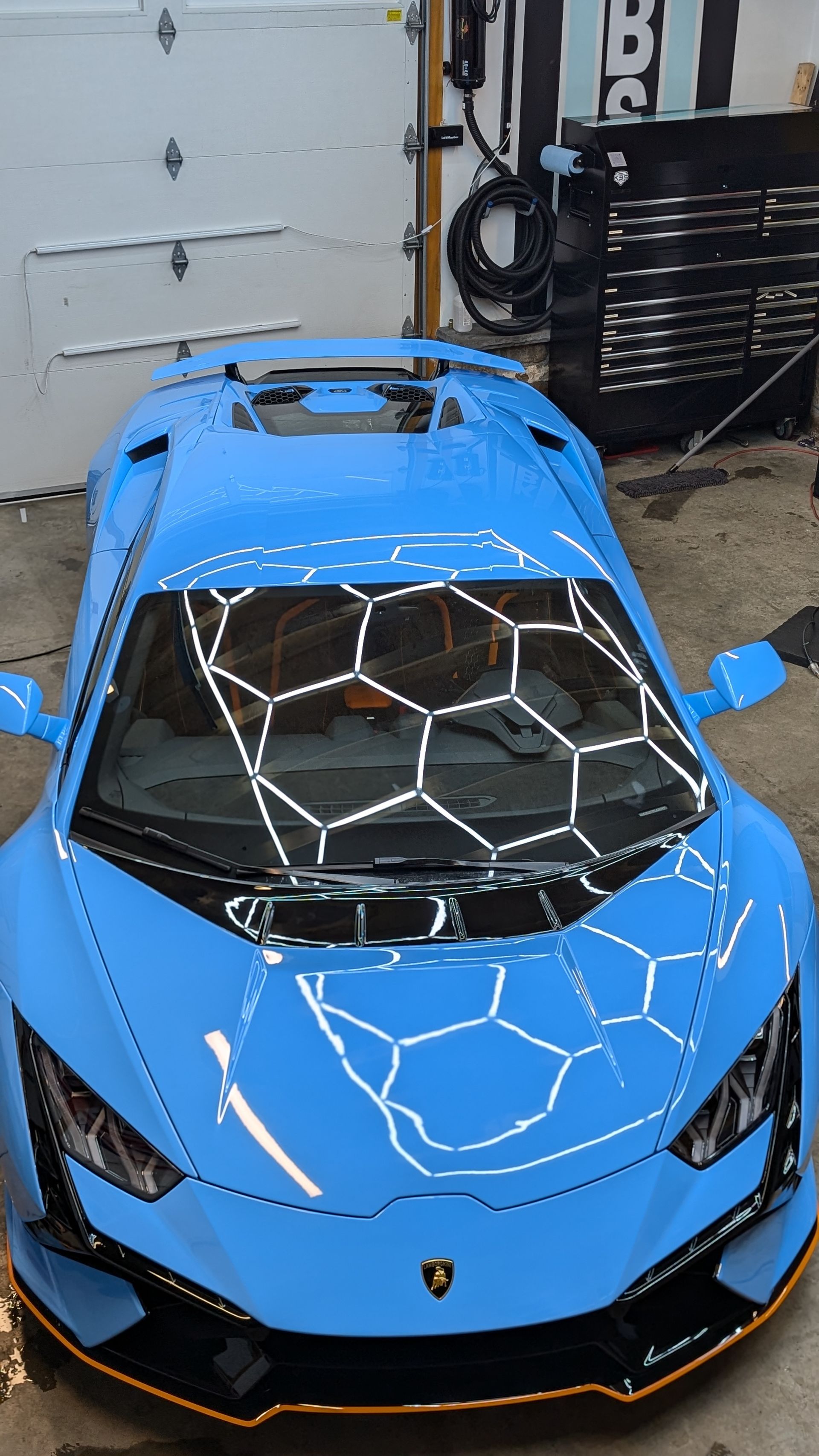 Bright blue Lamborghini sports car parked indoors, viewed from above, with a cracked windshield reflection.