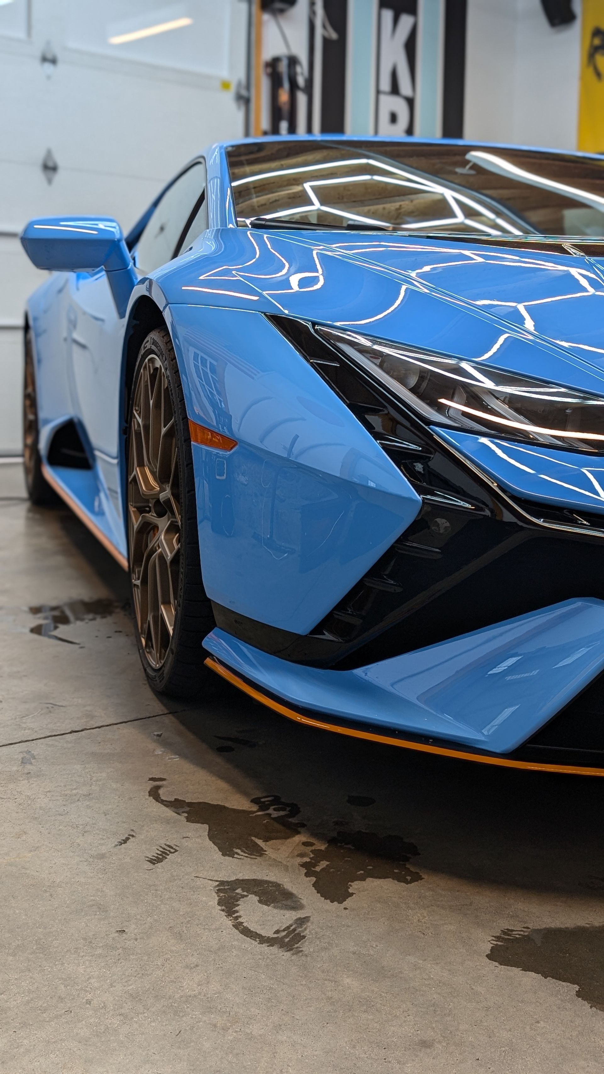 Blue sports car in a garage, front-left view, with sleek angular headlights and black/orange trim.