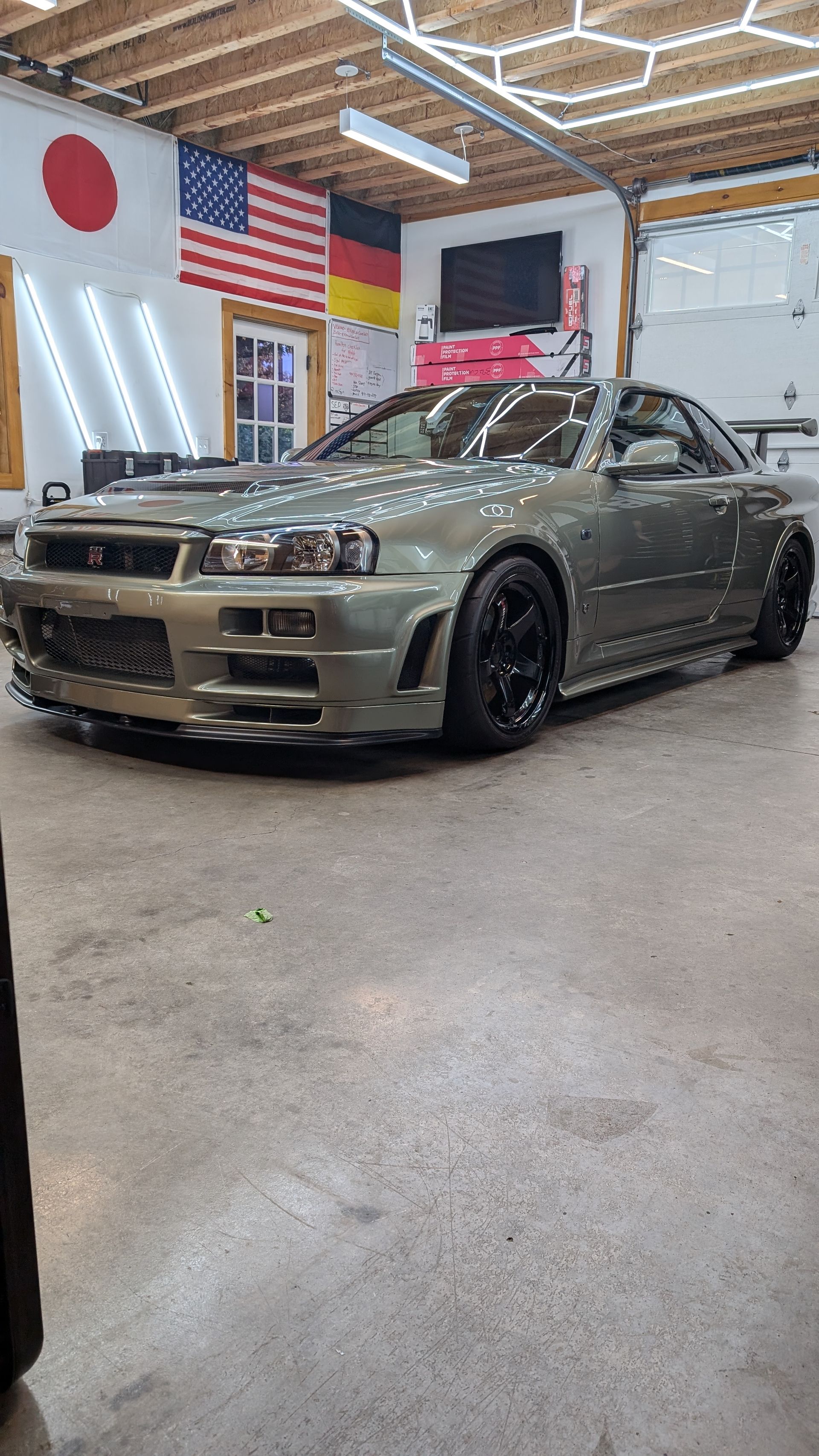 Modified silver sports car in a garage with Japanese and American flags on the wall