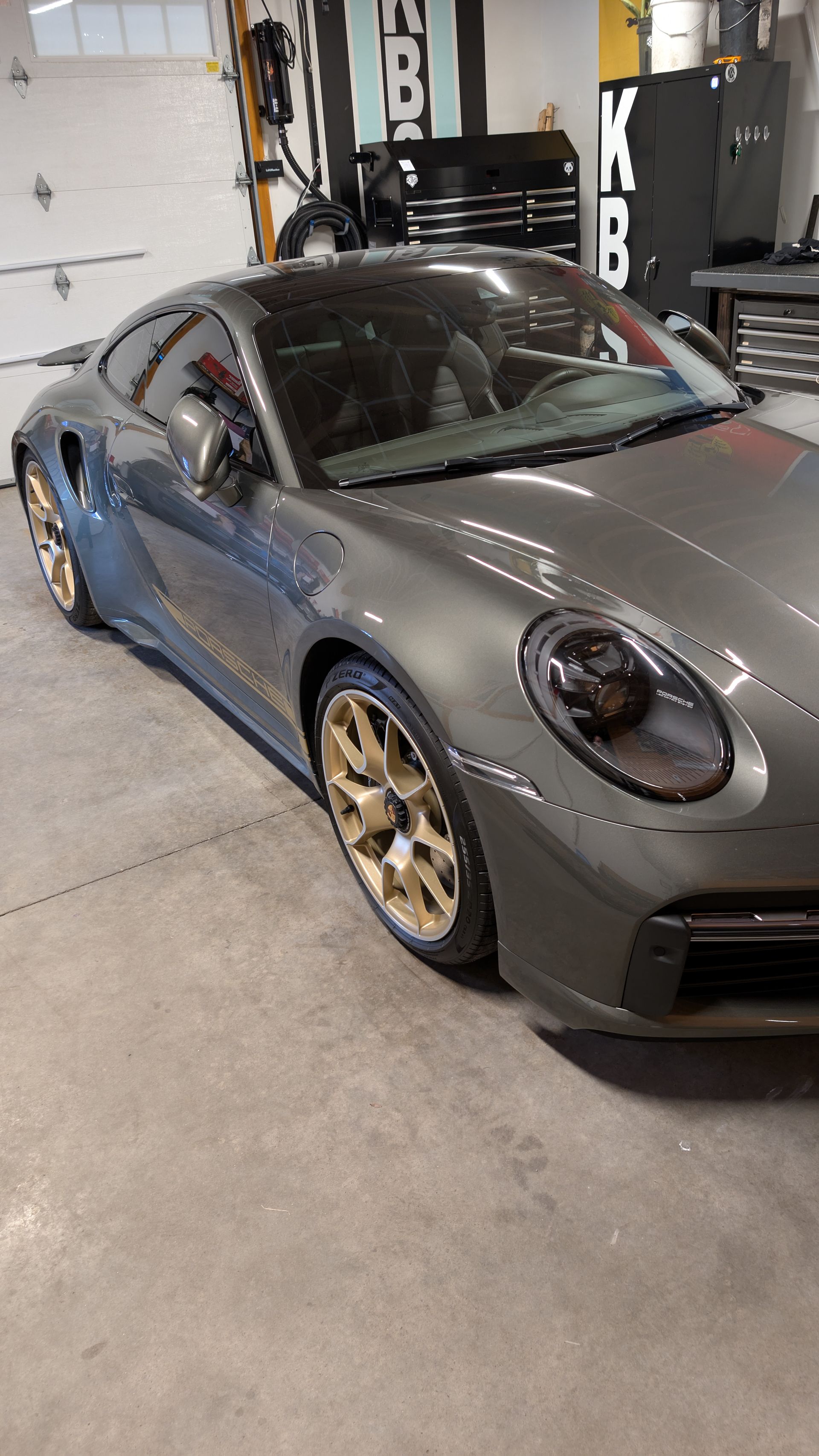 Gray sports car with gold wheels parked inside a garage or workshop.