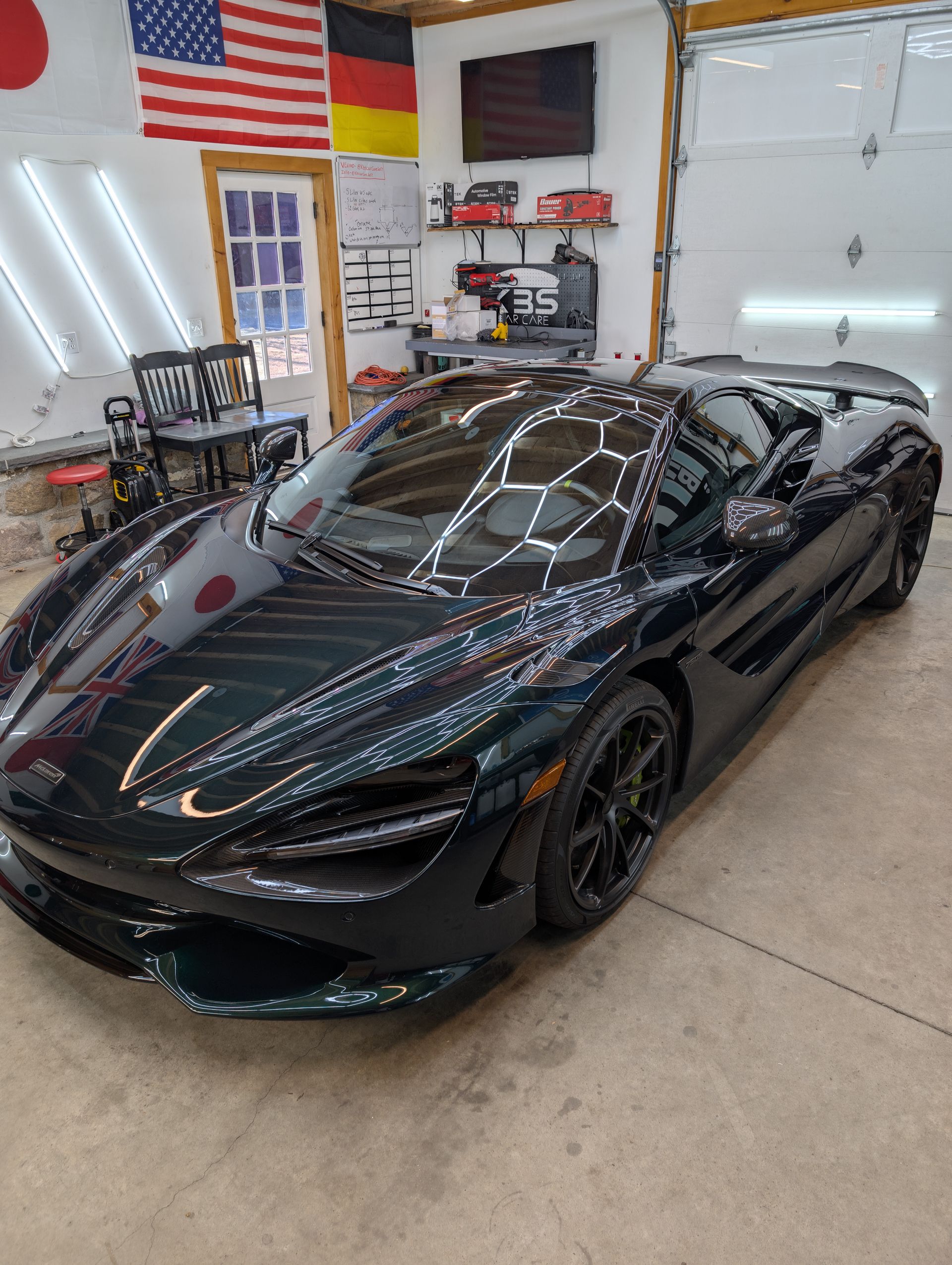 Black sports car in a garage with an American flag and tools in the background