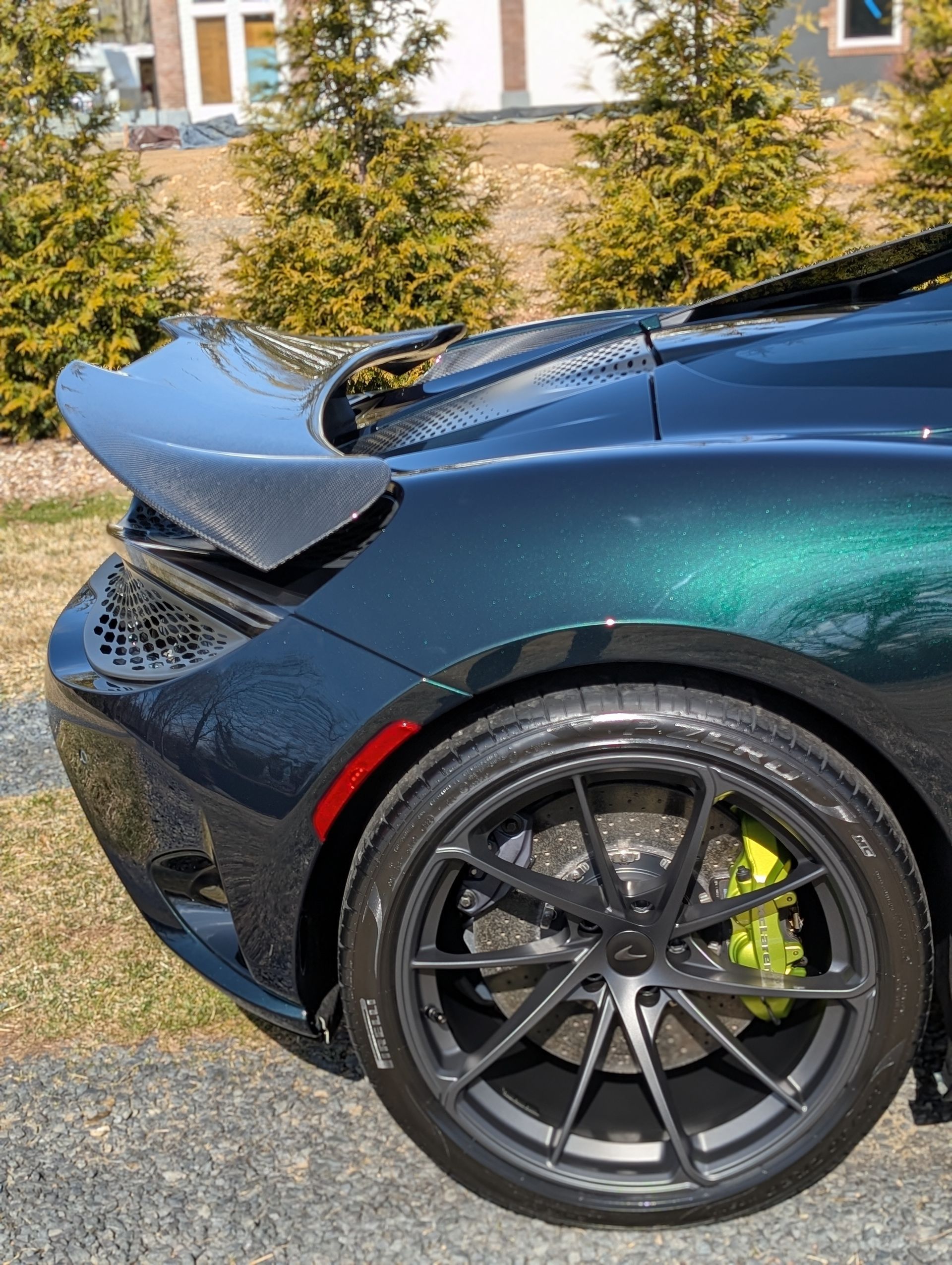 Close-up of a dark green sports car rear wheel and spoiler, parked outdoors.