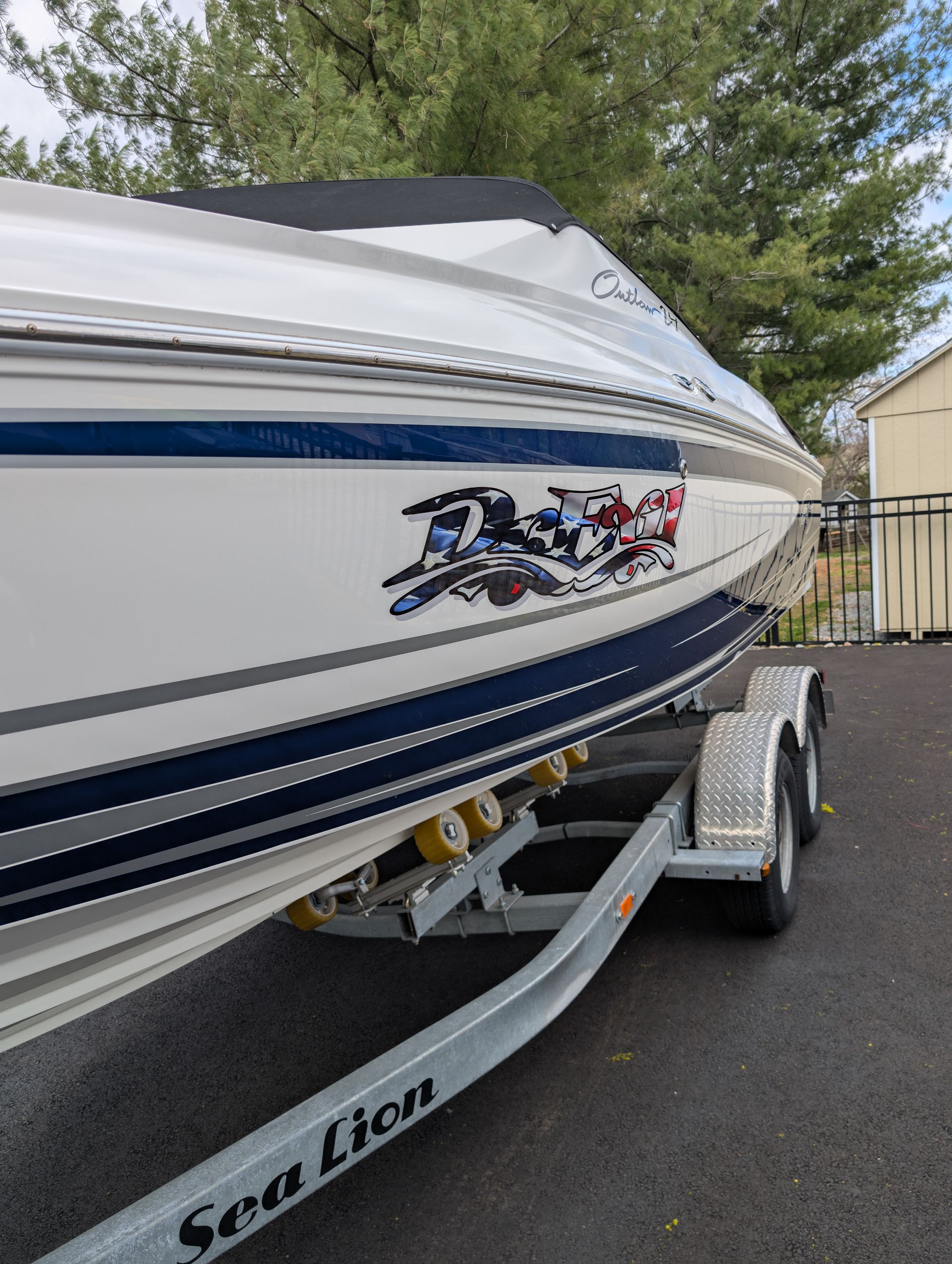 White Sea Lion speedboat on trailer, with blue accents and shark graphic, parked on a driveway.