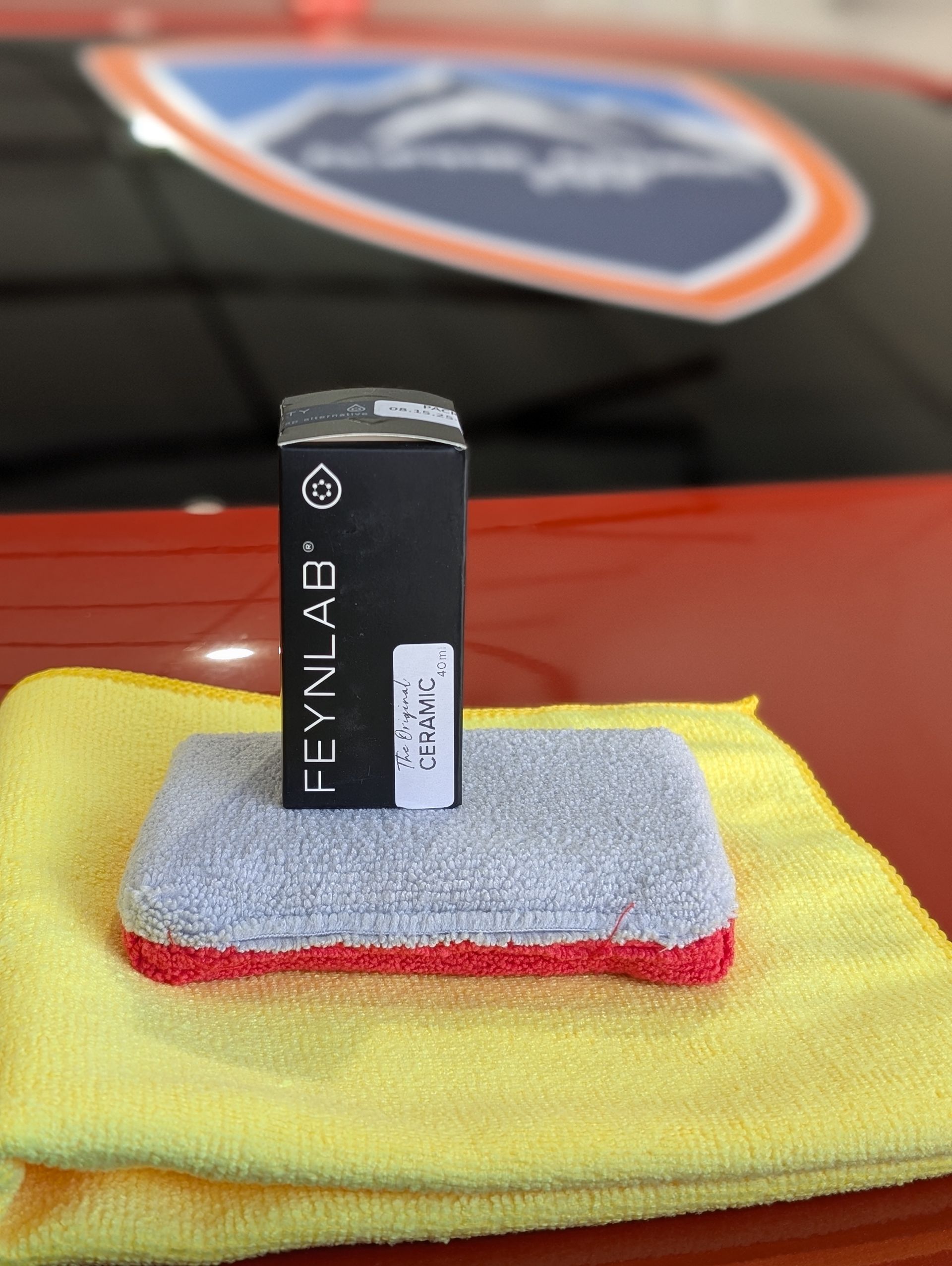 Small black and silver product box standing on a gray and red pad over a yellow cloth.