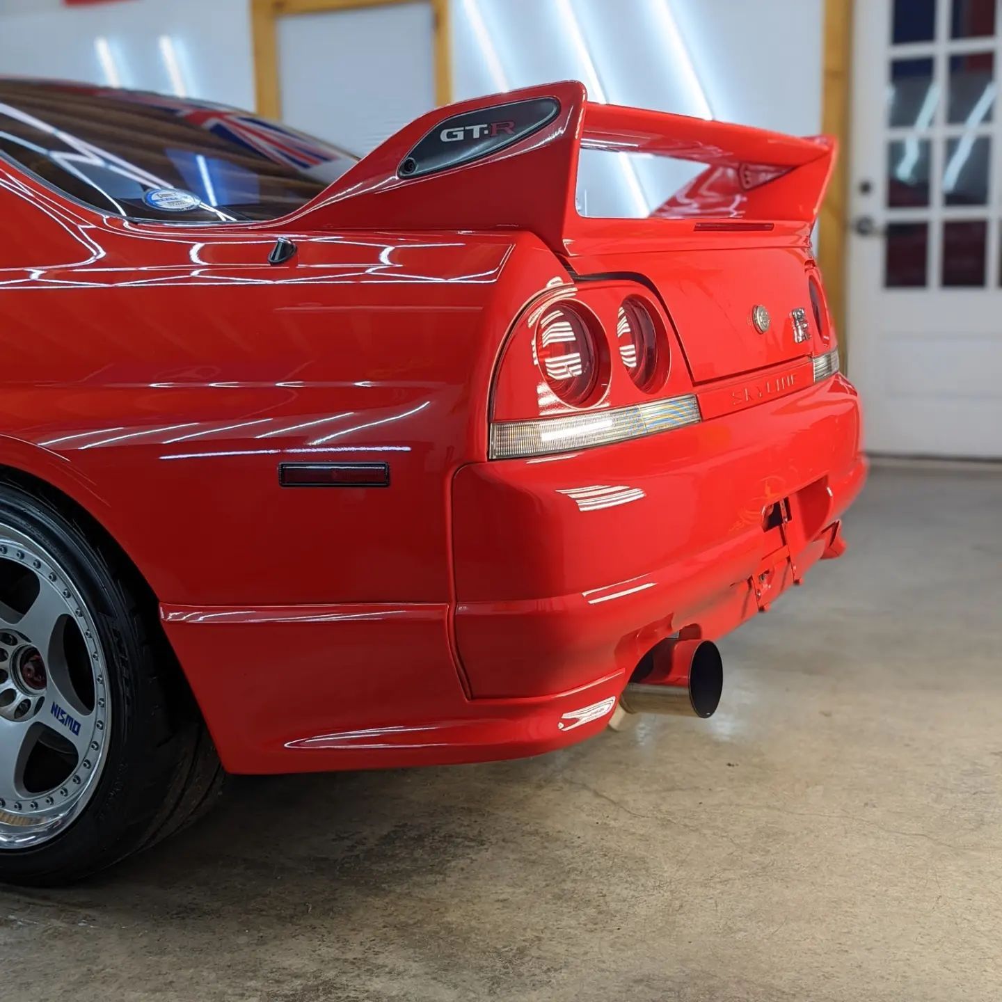 Red sports car rear quarter in a garage, with a spoiler and chrome tail lights.