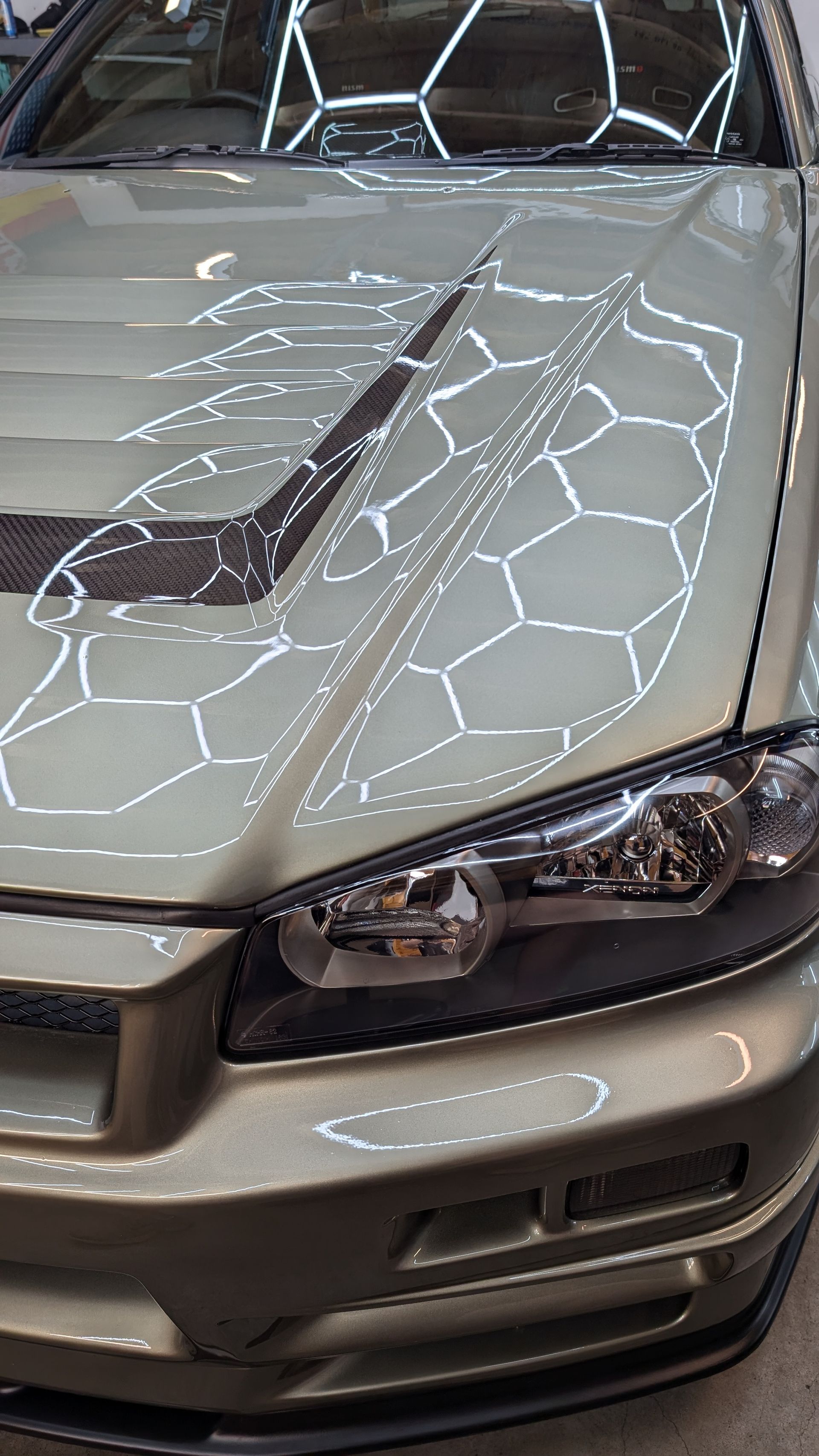 Front view of a beige car with a spiderweb crack across the hood and windshield.