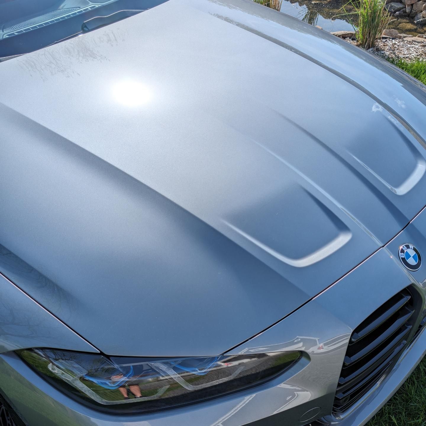 Close-up of a silver BMW hood and front headlight in sunlight