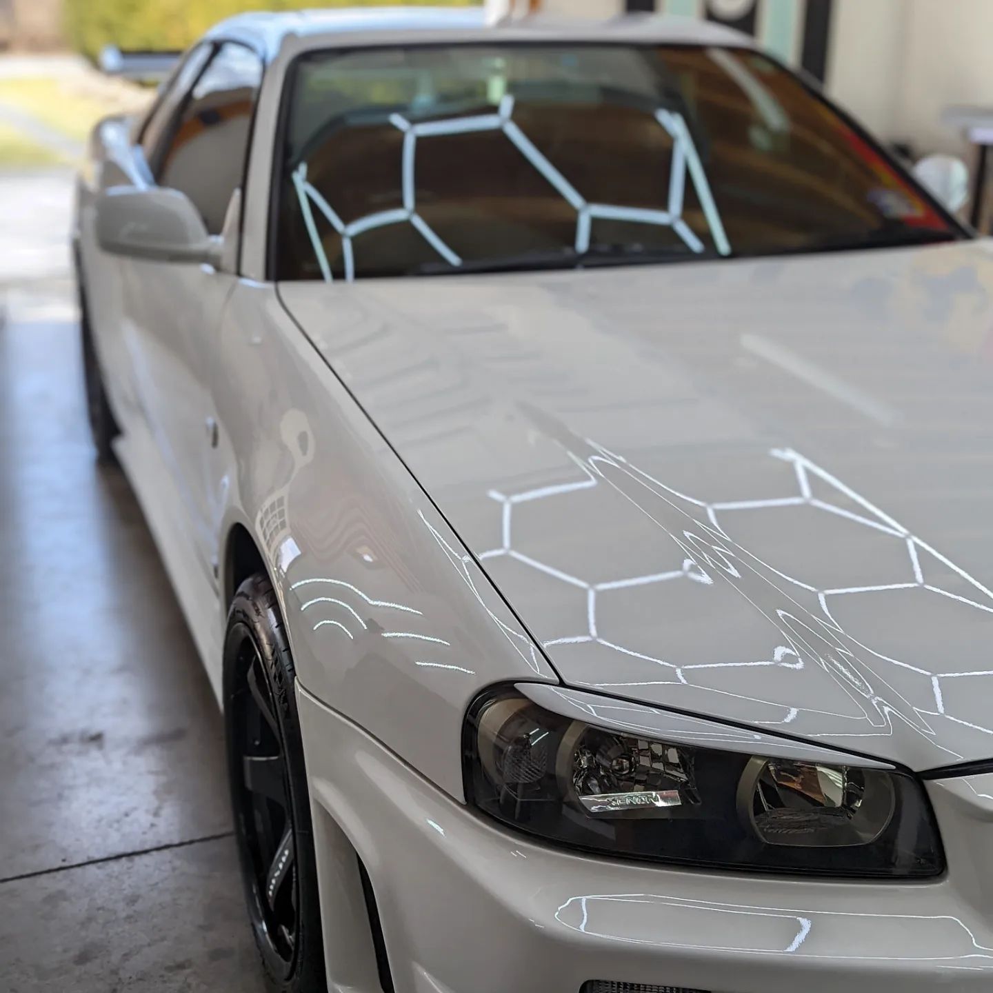 White sports car with black rims parked indoors, with geometric light reflections on the hood and windshield