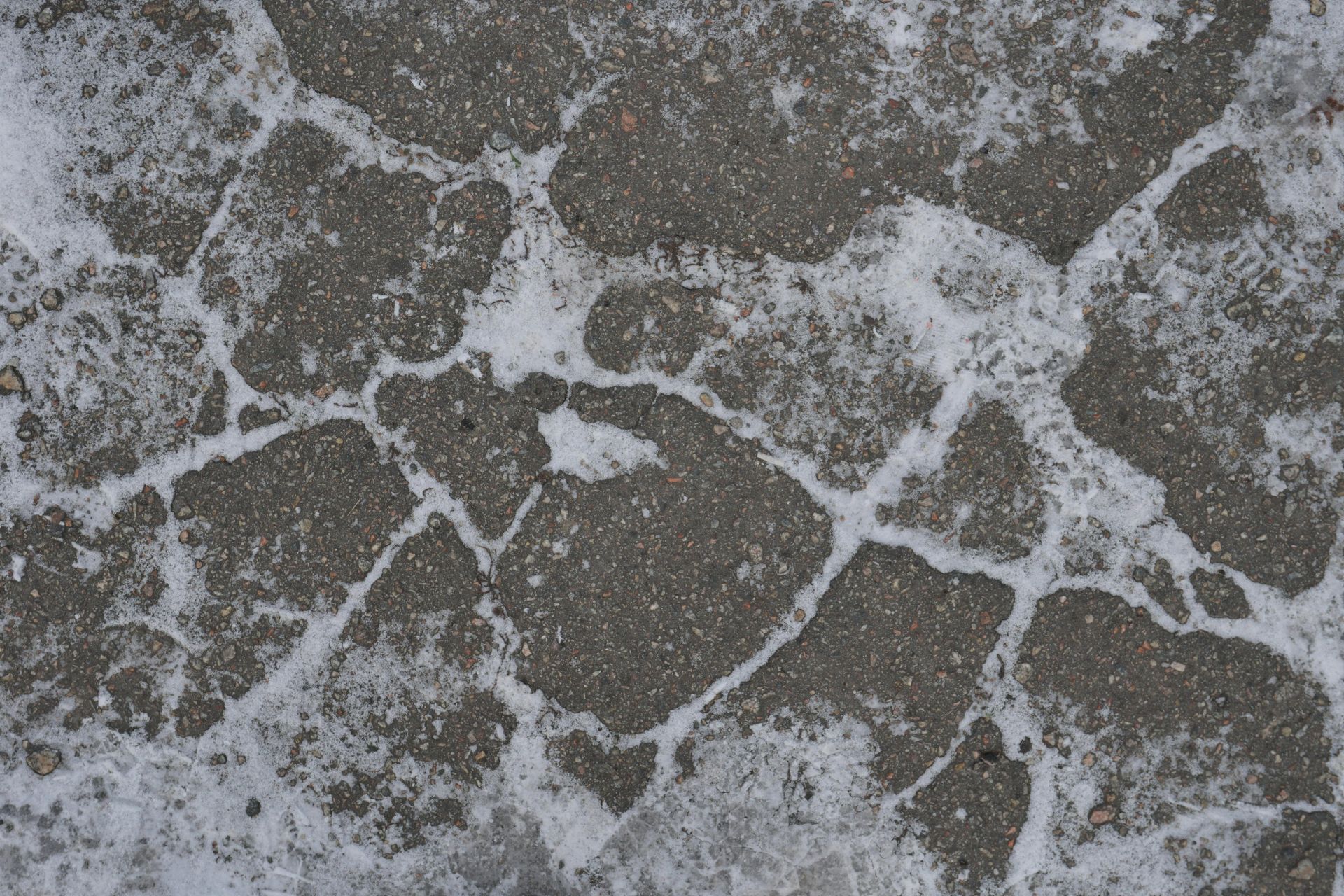 A close-up of cracked asphalt with white, granular snow or ice filled in the gaps.