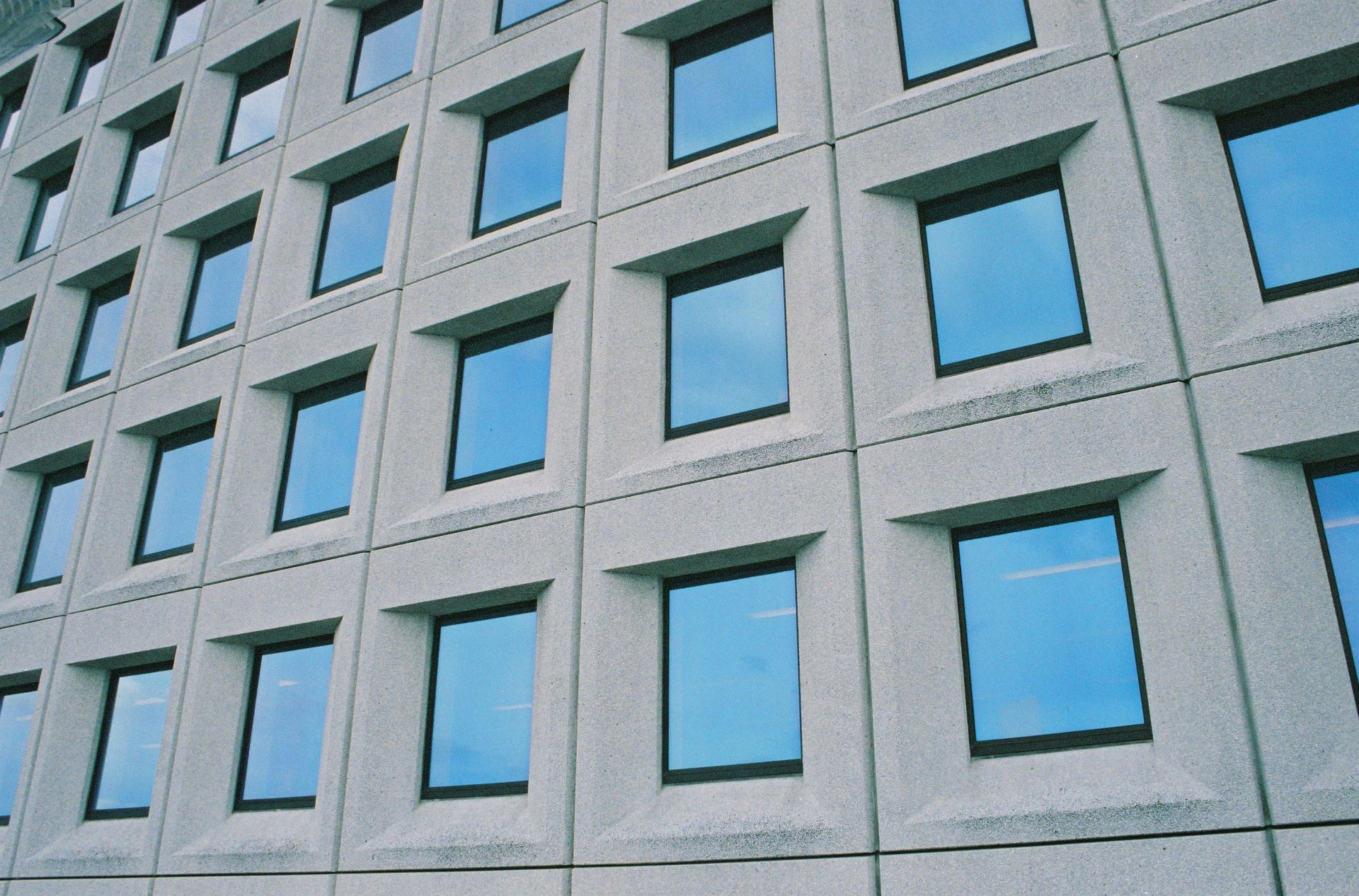 Modern building facade with rows of blue-tinted windows and gray concrete panels