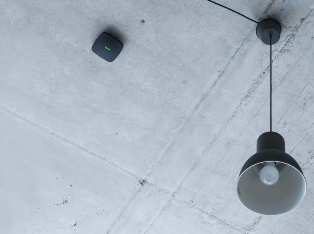 A Black Pendant Light Fixture And A Small, Square Black Sensor With A Faint Green Light Mounted On A Concrete Ceiling — Cussler NQ in Cannonvale, QLD