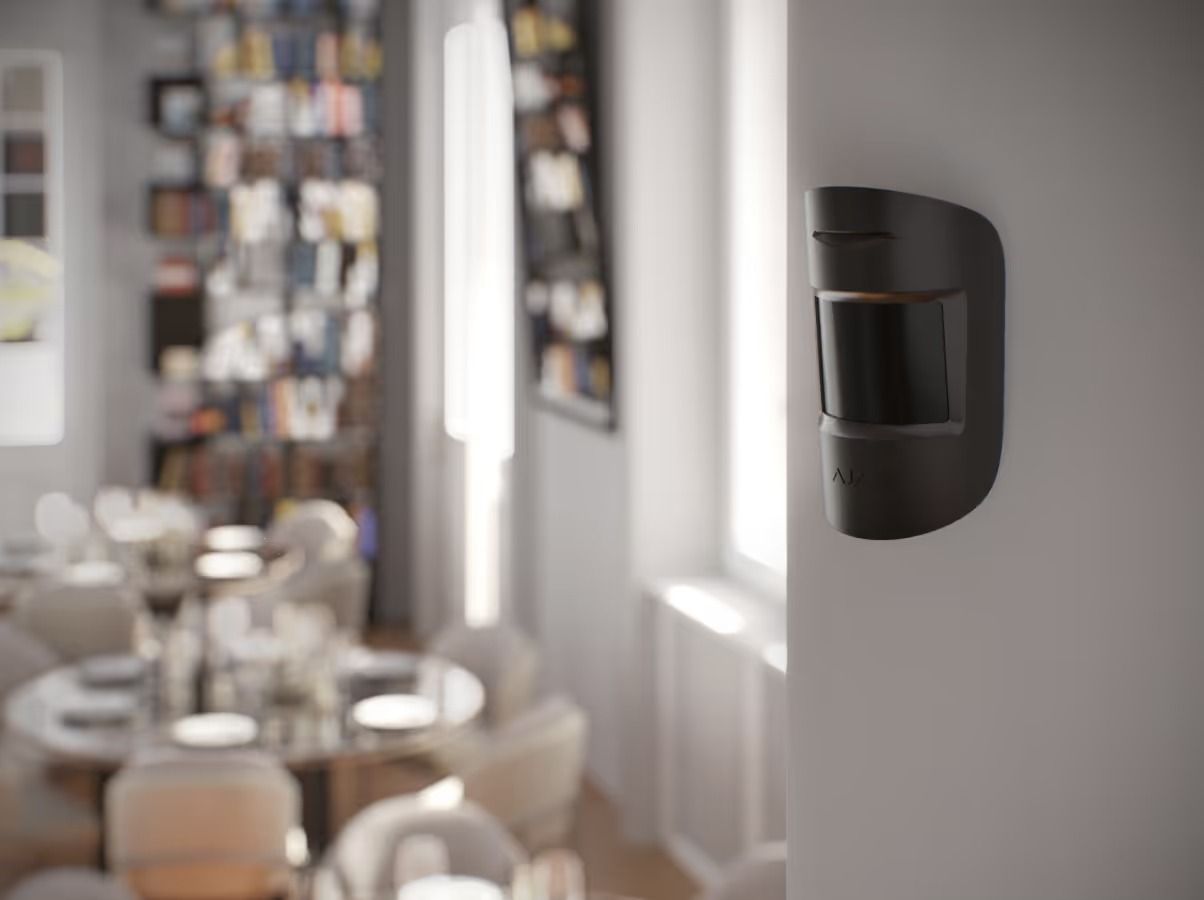 Dark-coloured Motion Sensor Mounted on a White Wall Inside a Room, With a Dining Area — Cussler NQ in Cannonvale, QLD