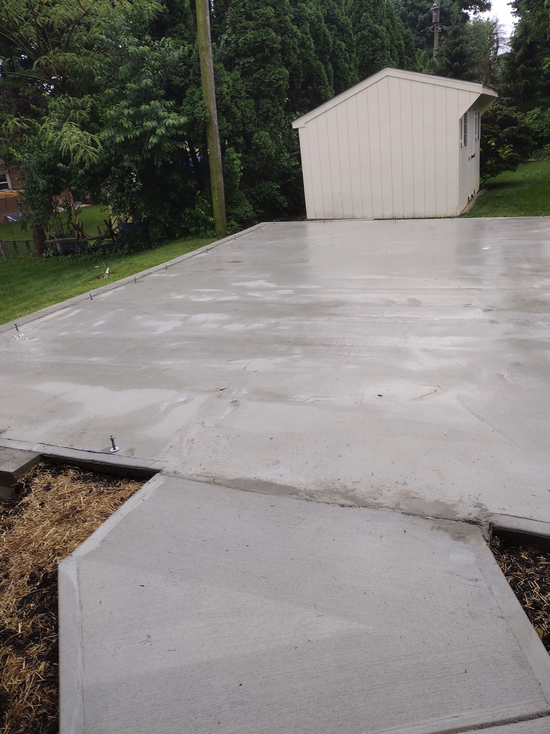 A newly poured concrete driveway and walkway leading to a small shed in a grassy backyard.
