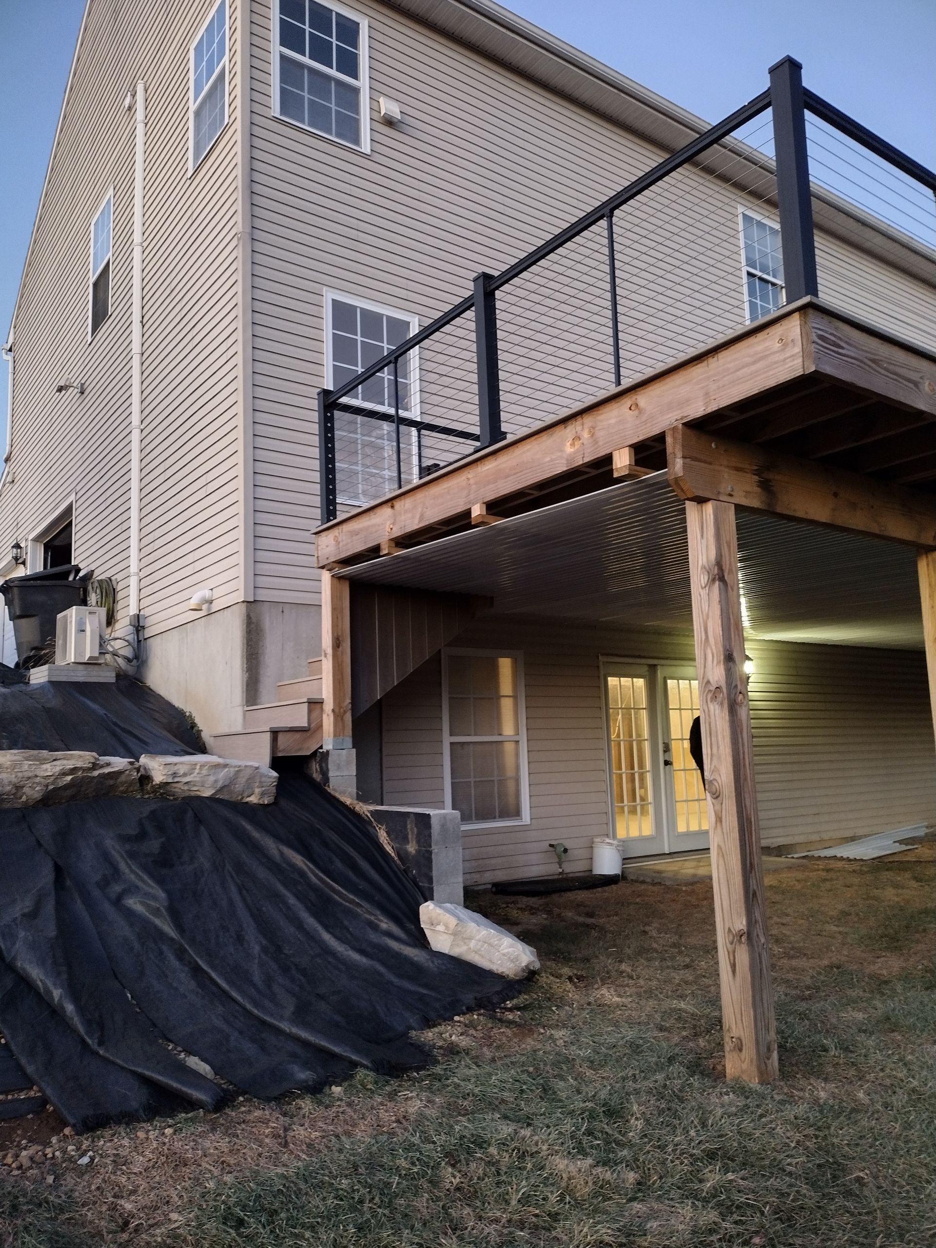 Exterior of a beige house featuring an elevated wooden deck with black railings above a walk-out basement patio.