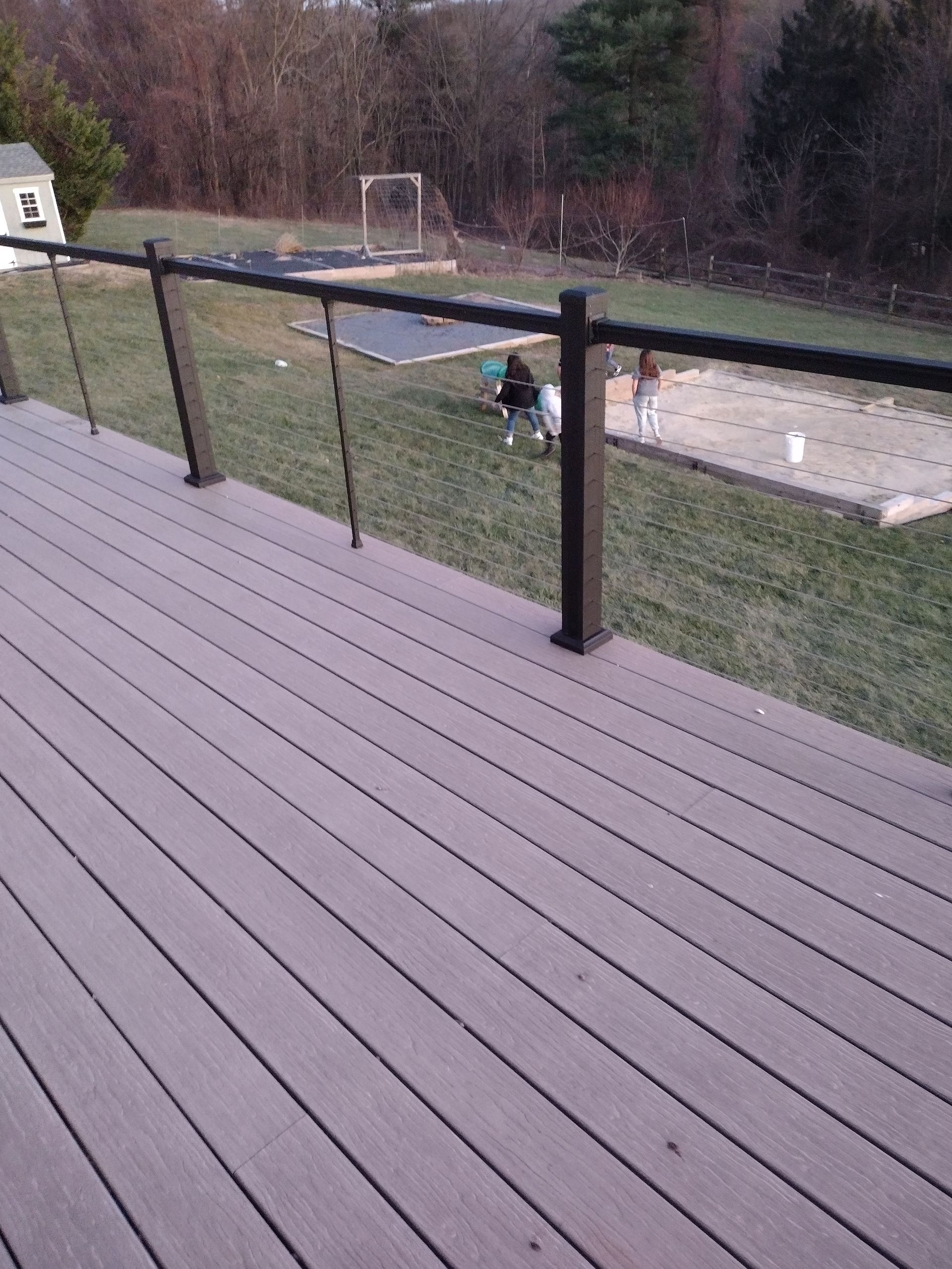 A view from a wooden deck looking out onto a backyard where two people are standing near a garden plot.