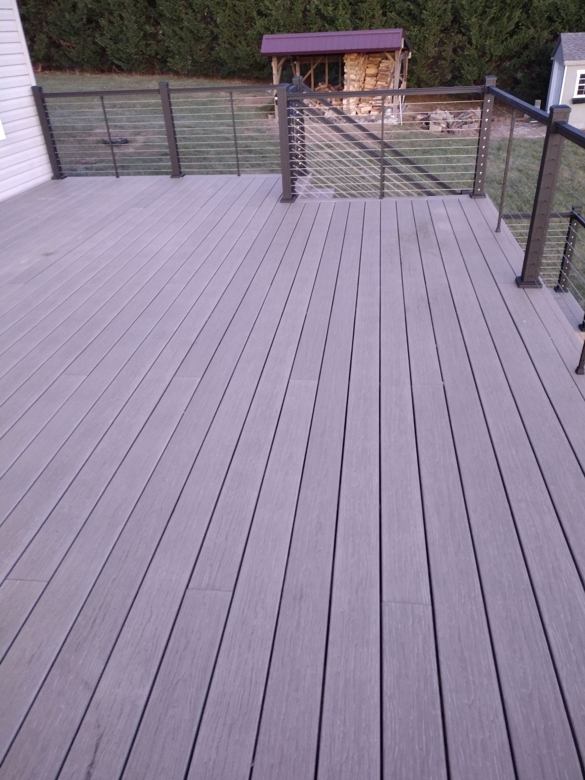 A gray composite deck with a modern railing overlooks a backyard with a small wooden structure.