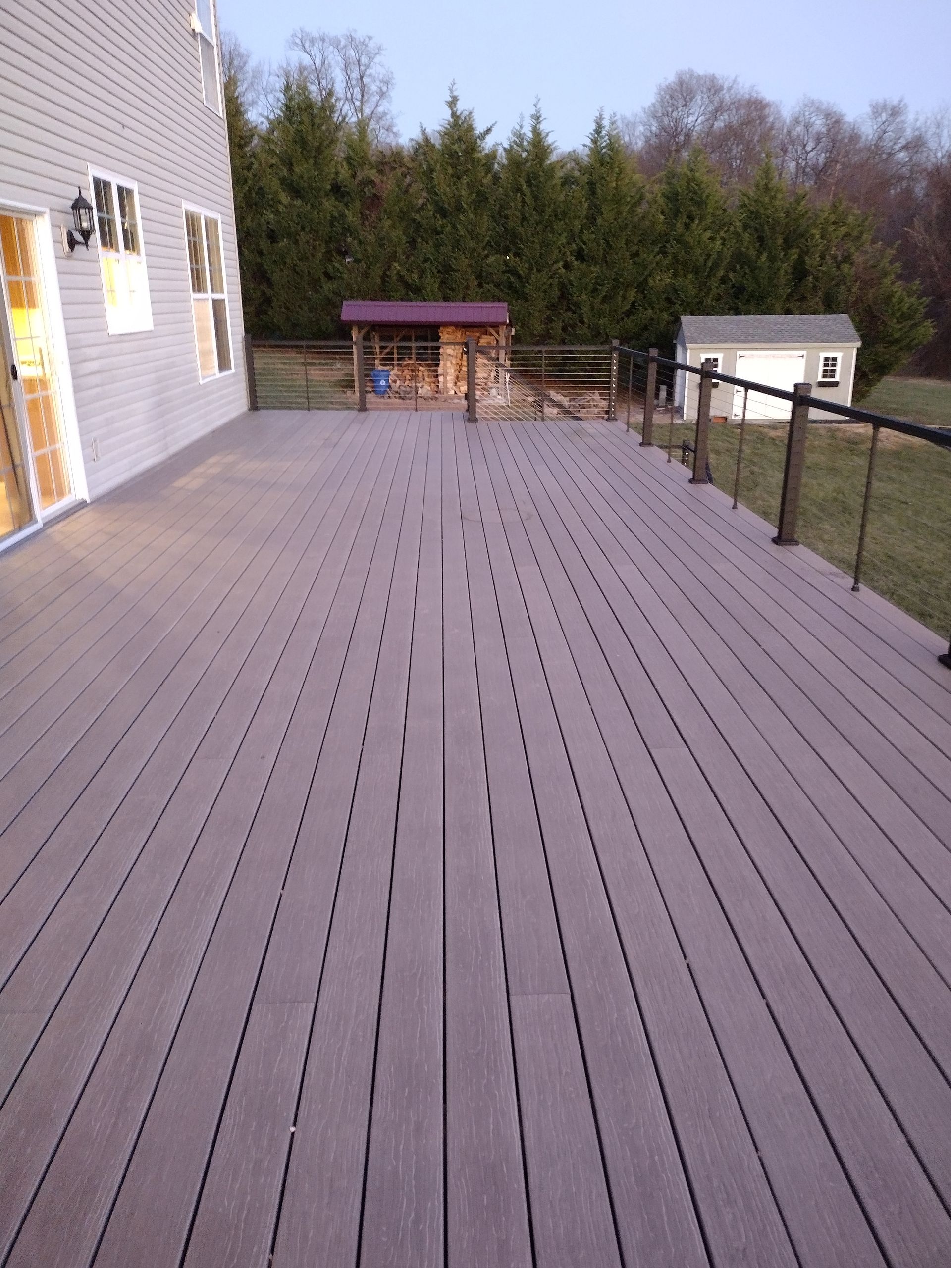 A spacious grey composite deck extends from a house, featuring a central seam and a railing overlooking a backyard.