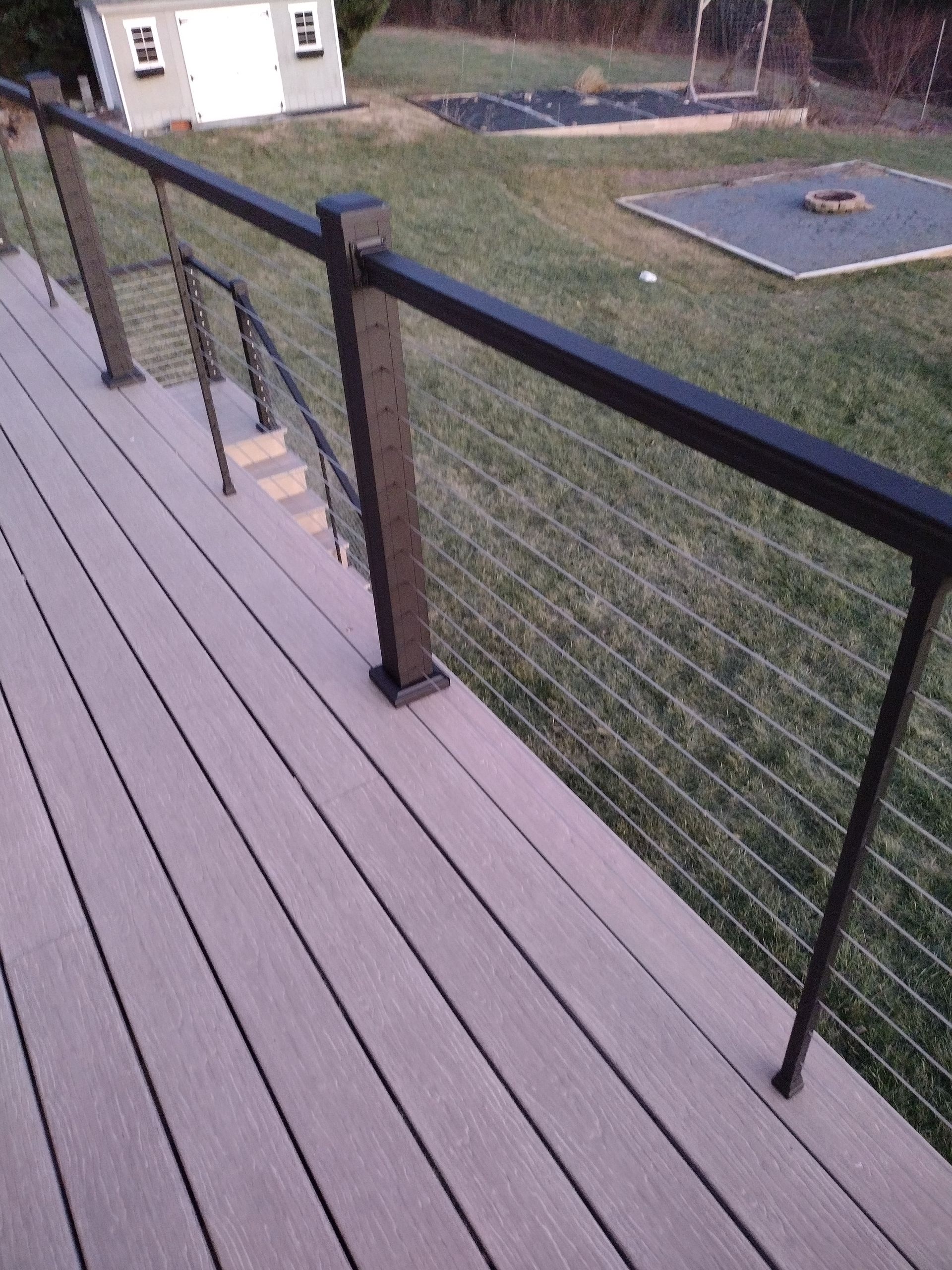 An elevated deck with composite light-colored planks and black metal railings with horizontal wire infill.