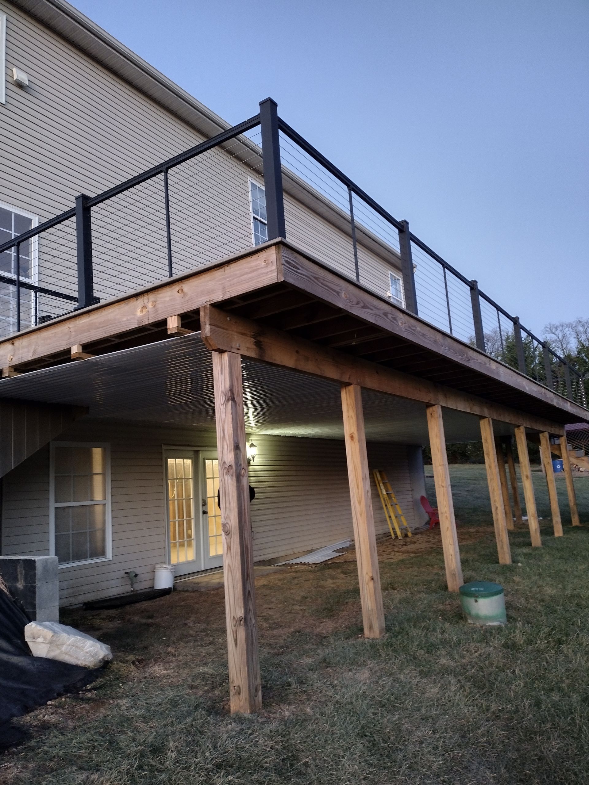 An elevated wooden deck with black railings over a lower patio area featuring French doors and vinyl siding.