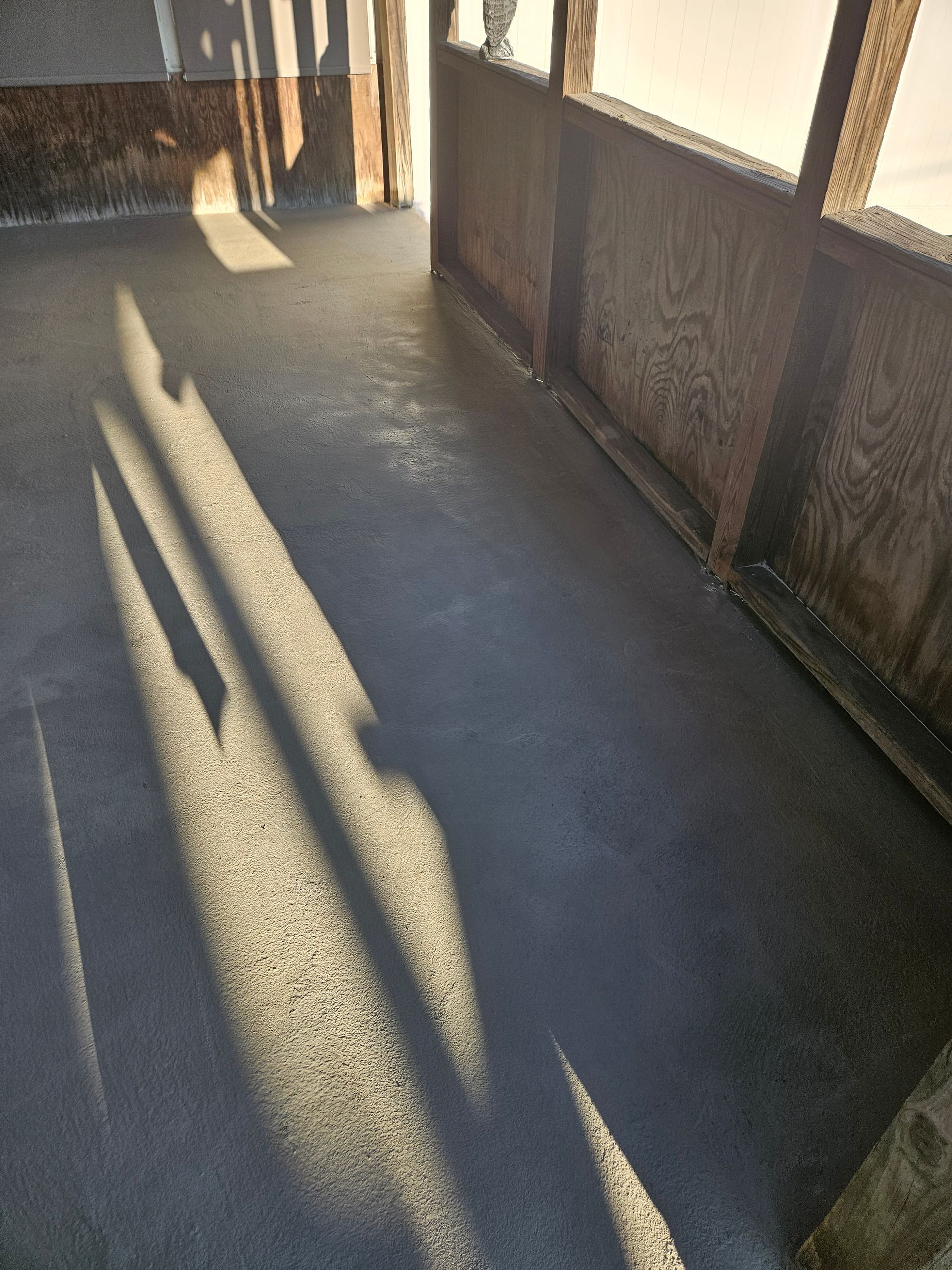 A freshly poured, smooth gray concrete floor inside a structure with wooden framing and wall panels.