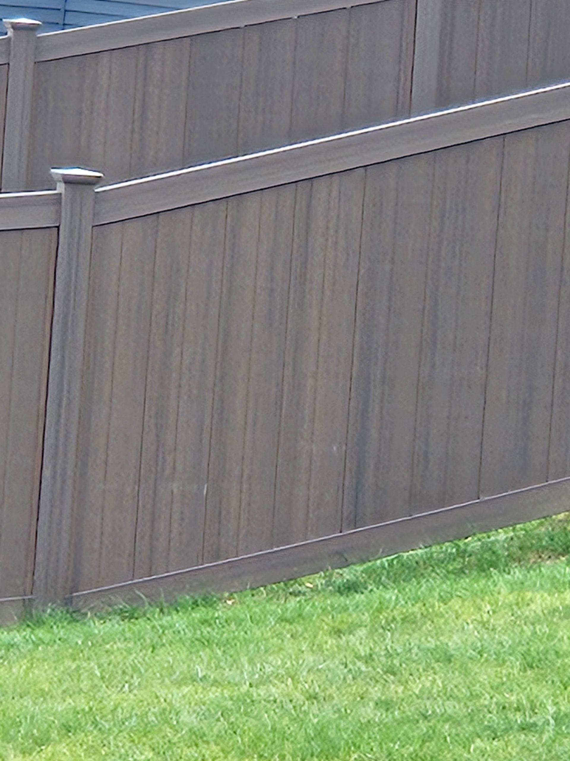A brown, vertically slatted vinyl privacy fence set against a green grass lawn.