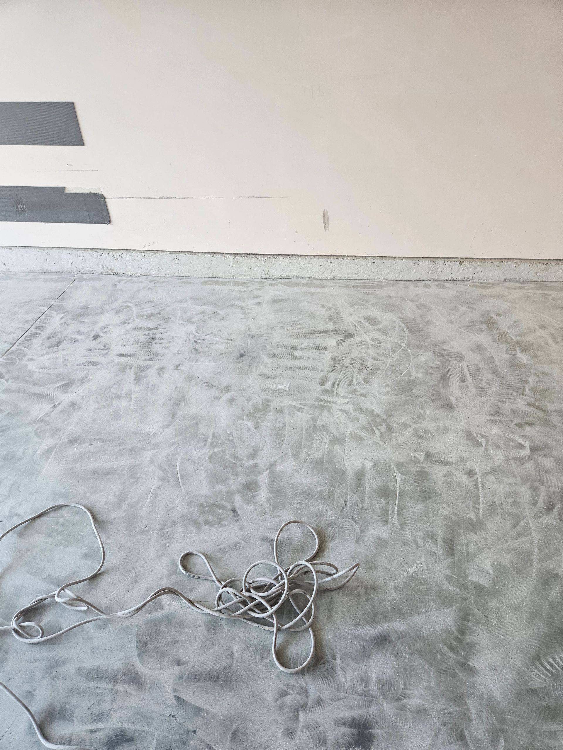 A tangled, silver-colored rope lies on a gray concrete floor in front of a plain, light-colored wall.
