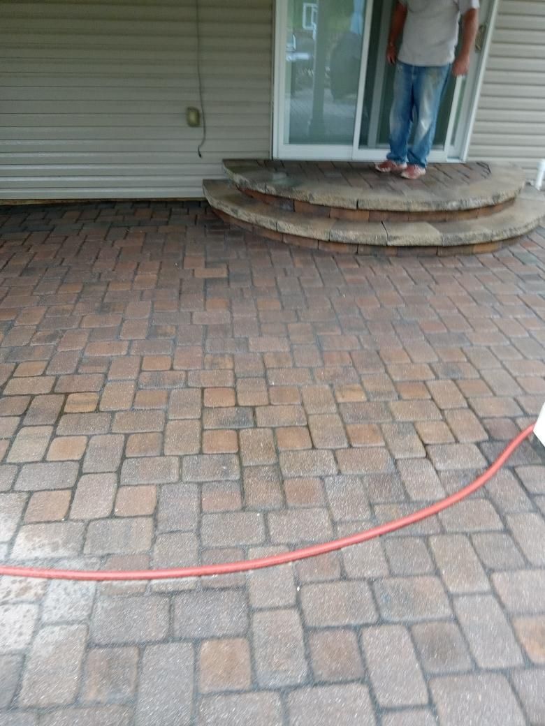A person stands on semicircular stone steps leading to a sliding door, overlooking a multi-colored stone paver patio.
