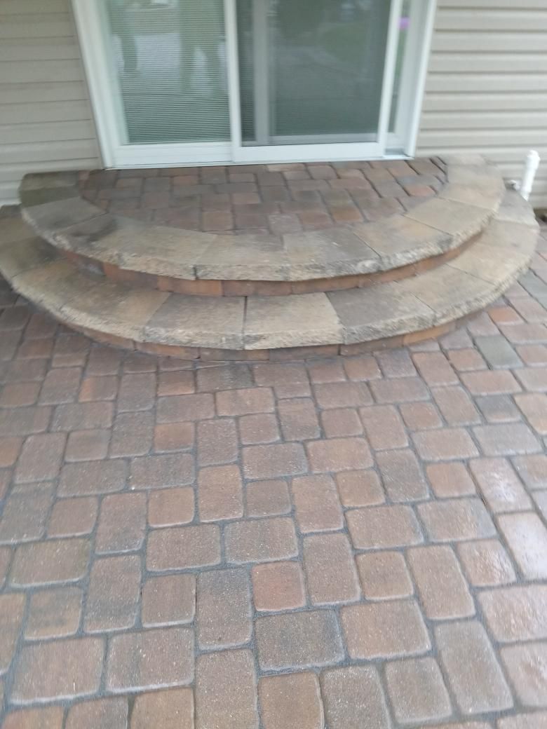 Two semi-circular stone steps leading to a sliding glass door on a paved patio.