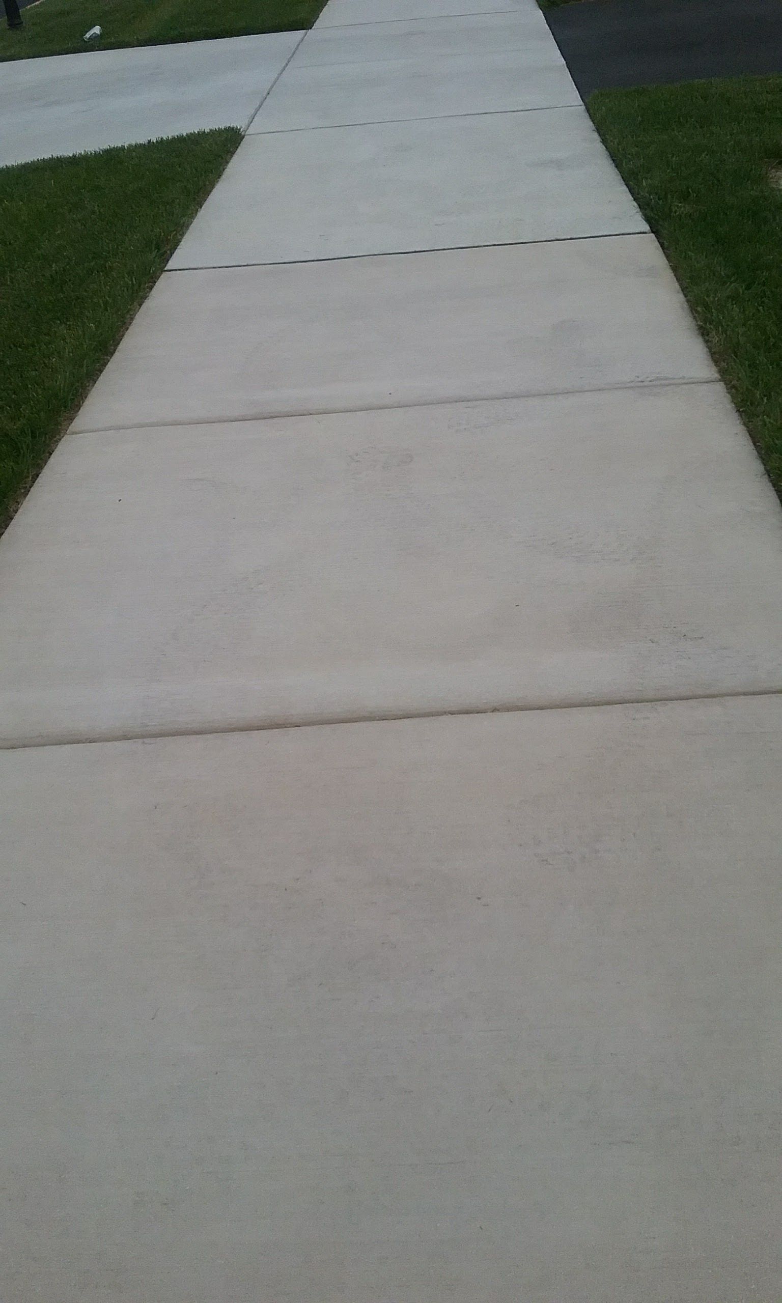 A straight concrete sidewalk stretches into the distance, bordered by green grass on both sides.
