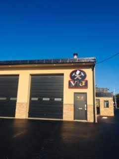 A tan commercial building with two large black garage doors and a sign featuring crossed hammers under a blue sky.