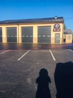 A low-angle view of a beige commercial building with three dark garage doors and a logo above a side door in a parking lot.