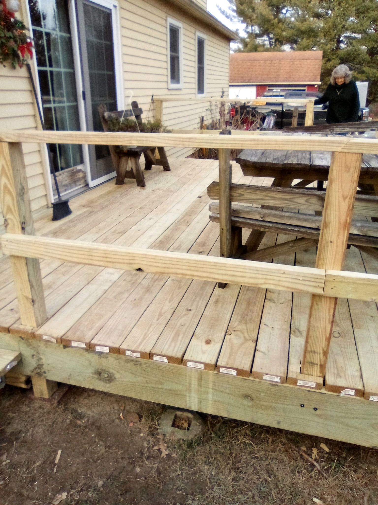 A newly built wooden deck with a simple railing attached to the side of a light-colored house.