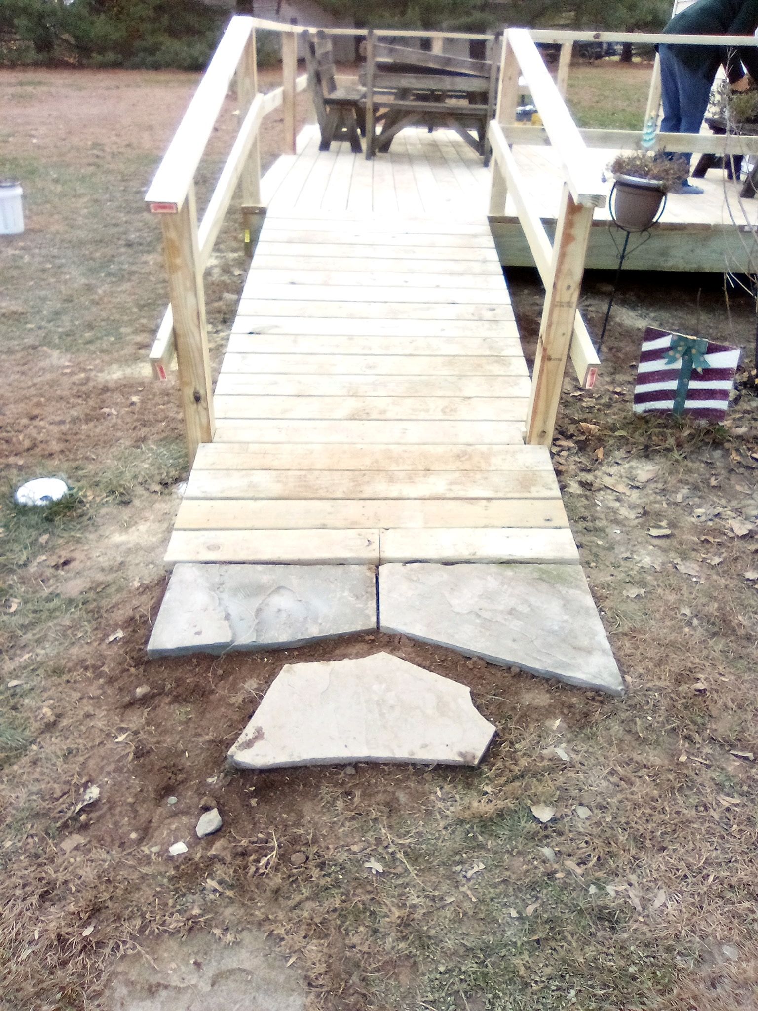 A wooden wheelchair ramp leading to a deck, with stone pavers placed at the base on a grassy ground.