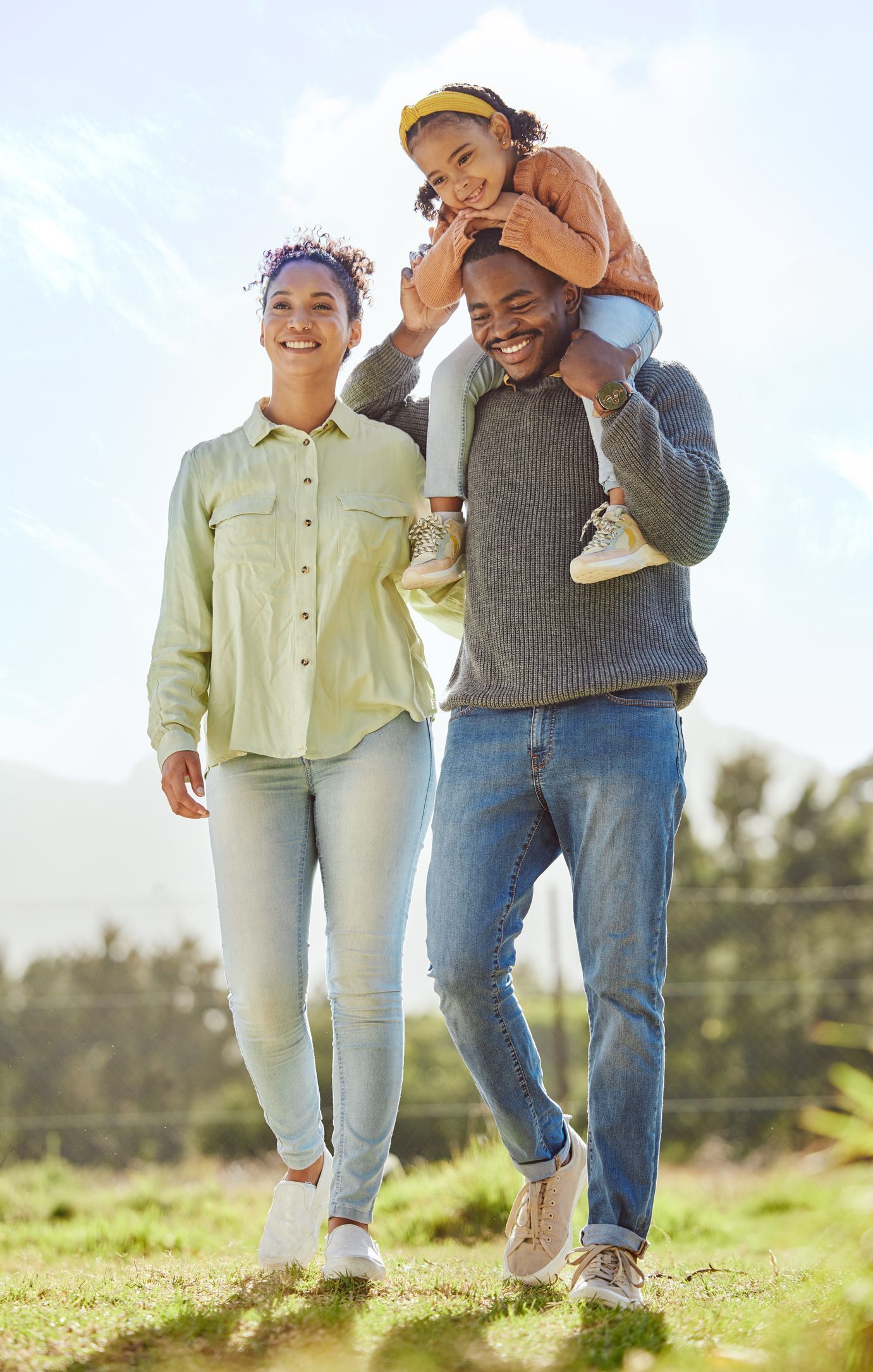 A father is carrying his young daughter on his shoulders next to his wife.