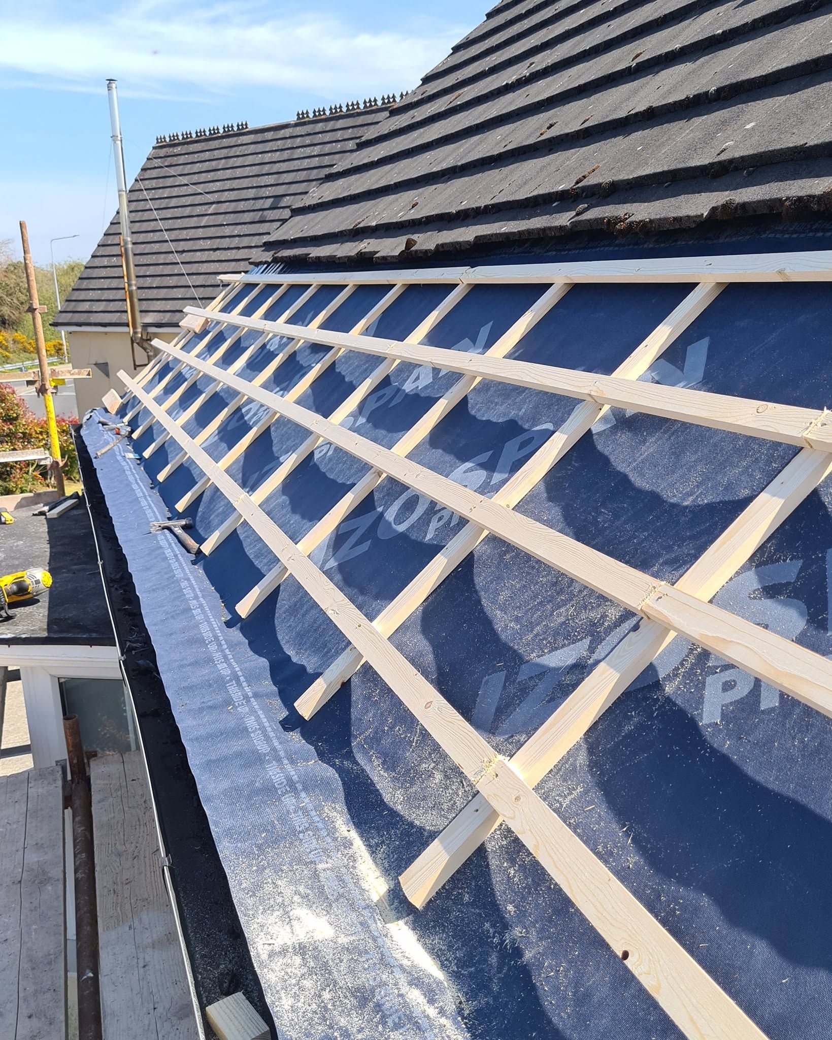 Roof under construction with wooden battens over blue waterproof membrane on a sloped house roof