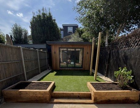 Backyard with wooden raised beds, green lawn, and a small shed or studio at the end of a narrow garden.