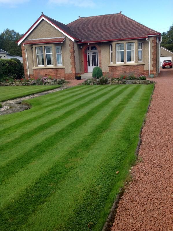 Brick house with striped green lawn and gravel driveway in front garden